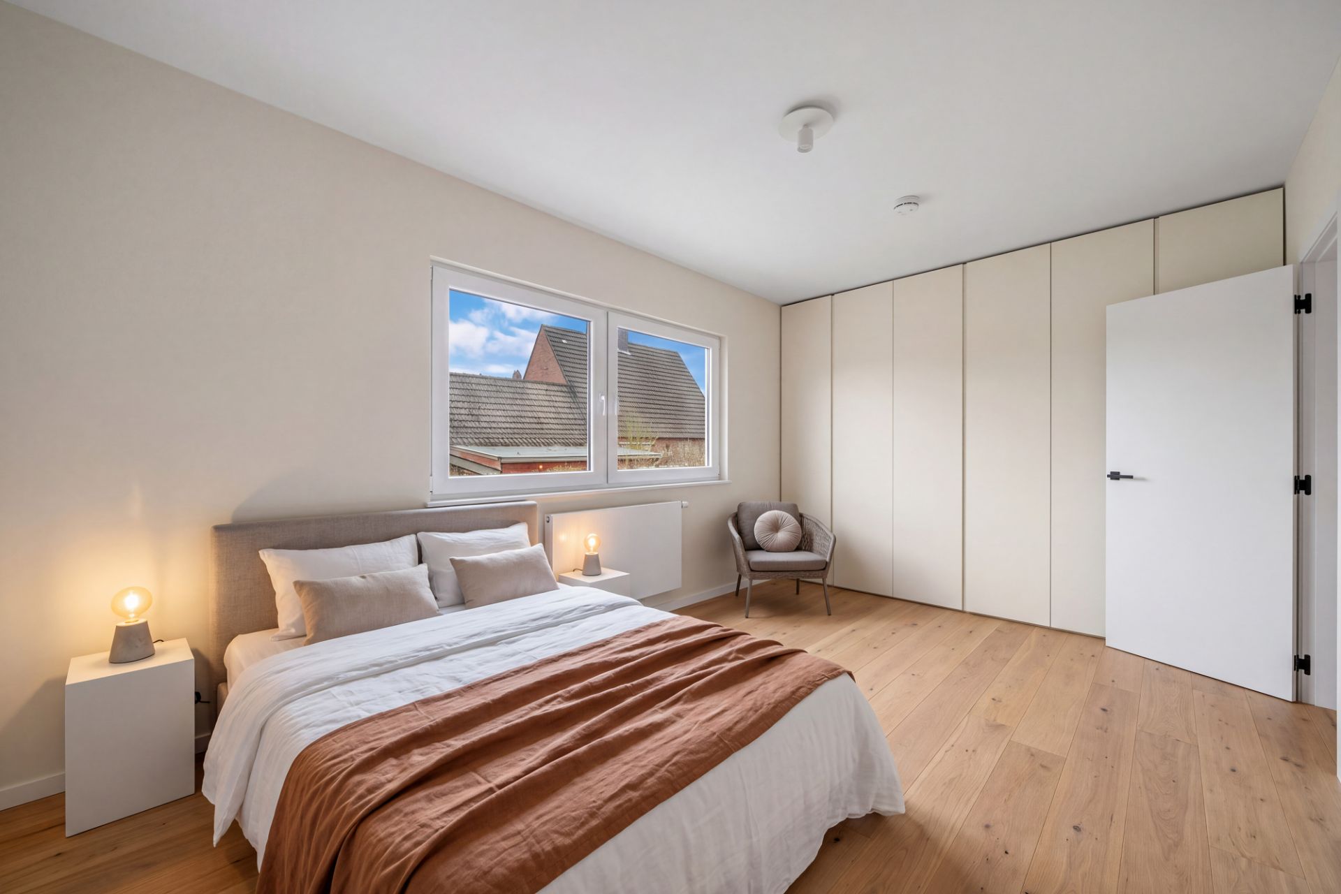 Helles Schlafzimmer mit großem Bett, Kleiderschrank, Stuhl und zwei Fenstern.