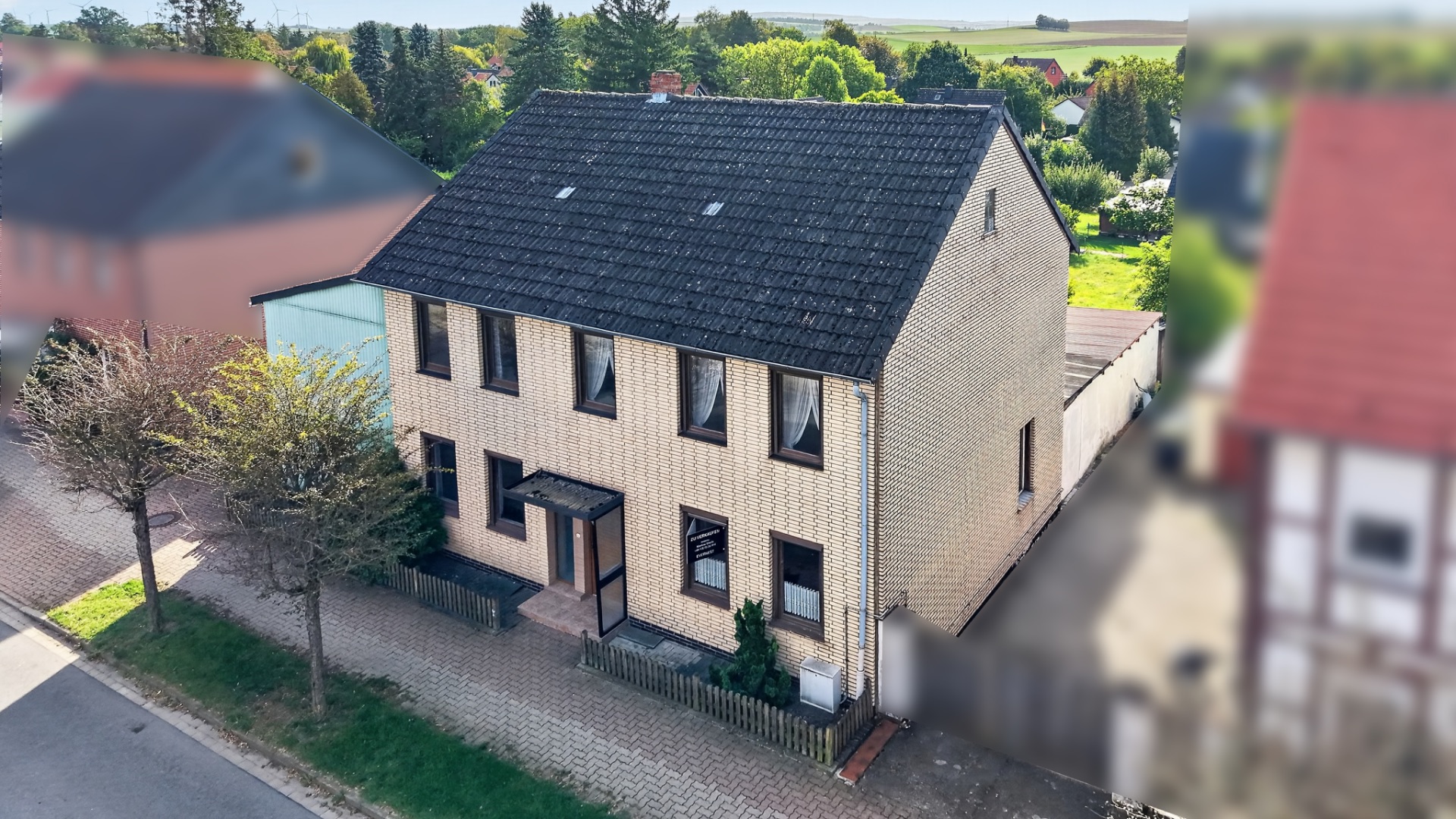 Zweistöckiges Einfamilienhaus mit hellem Klinker, Vorgarten und Gehweg, von oben aufgenommen.