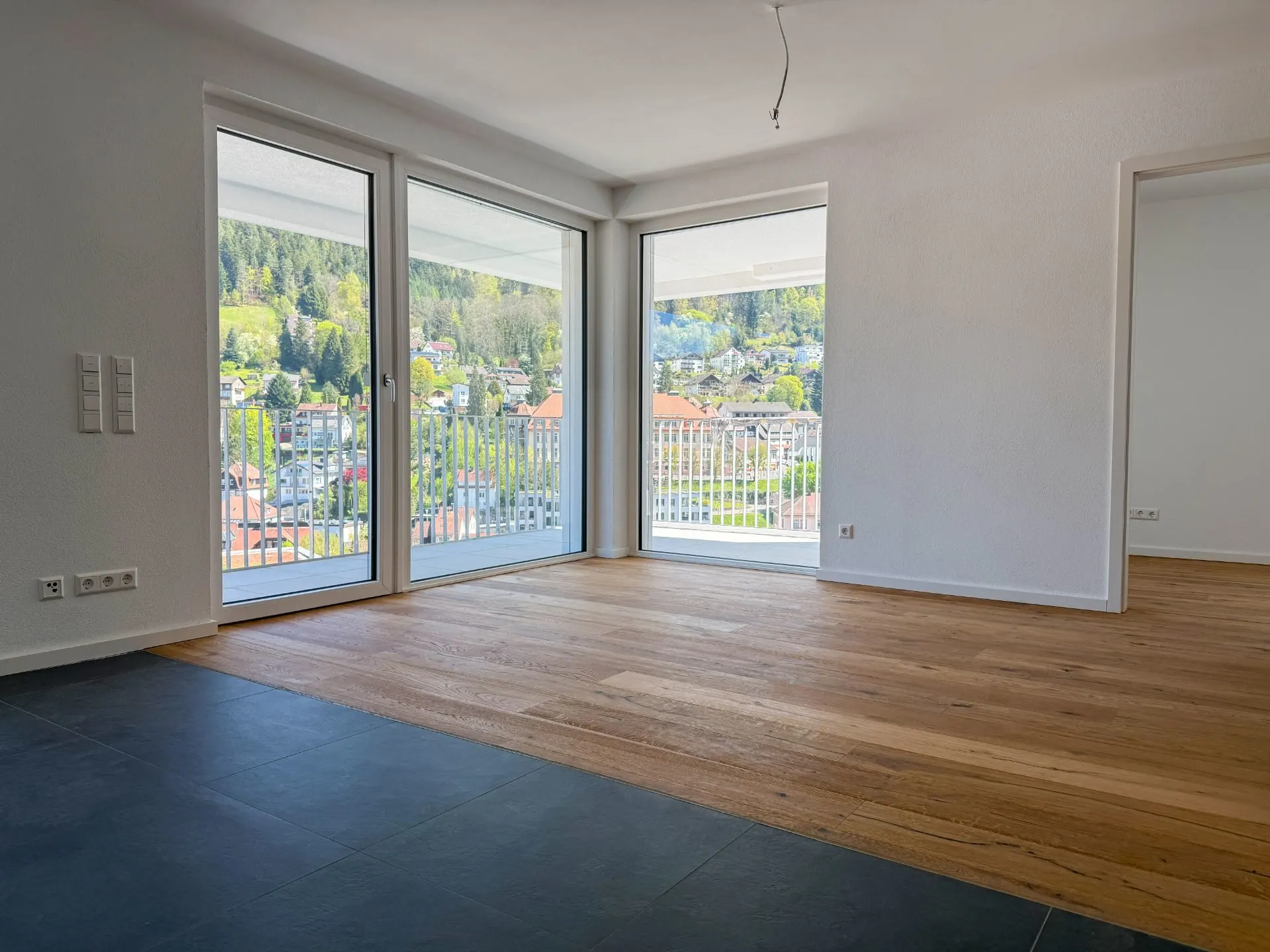 Helles Wohnzimmer mit großen Fenstern, Holzboden und Blick auf einen Balkon mit Aussicht.