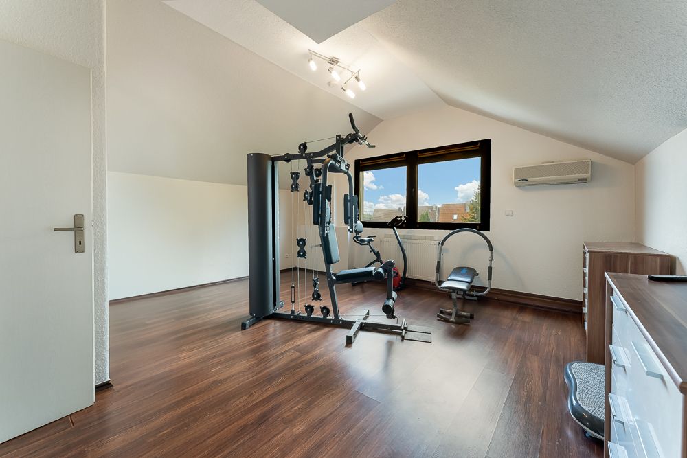 Heller Raum mit Sportgerät, Fitnessbank, Holzfußboden und großem Fenster.