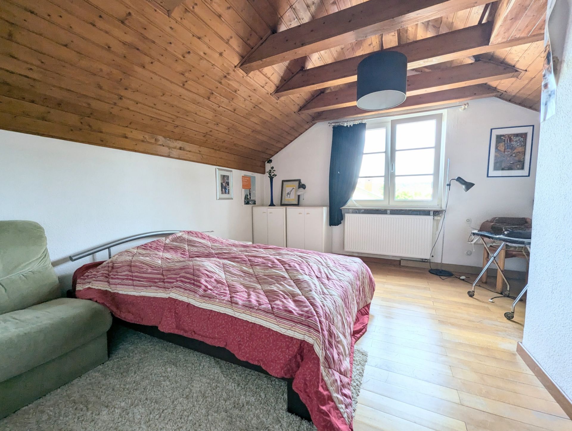 Dachzimmer mit Bett, Holzdecke, Fenster, Schrank und Sofa.