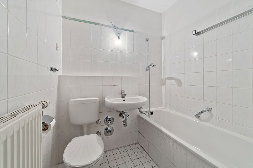 Helles Badezimmer mit Badewanne, WC, Waschbecken und weißen Fliesen.