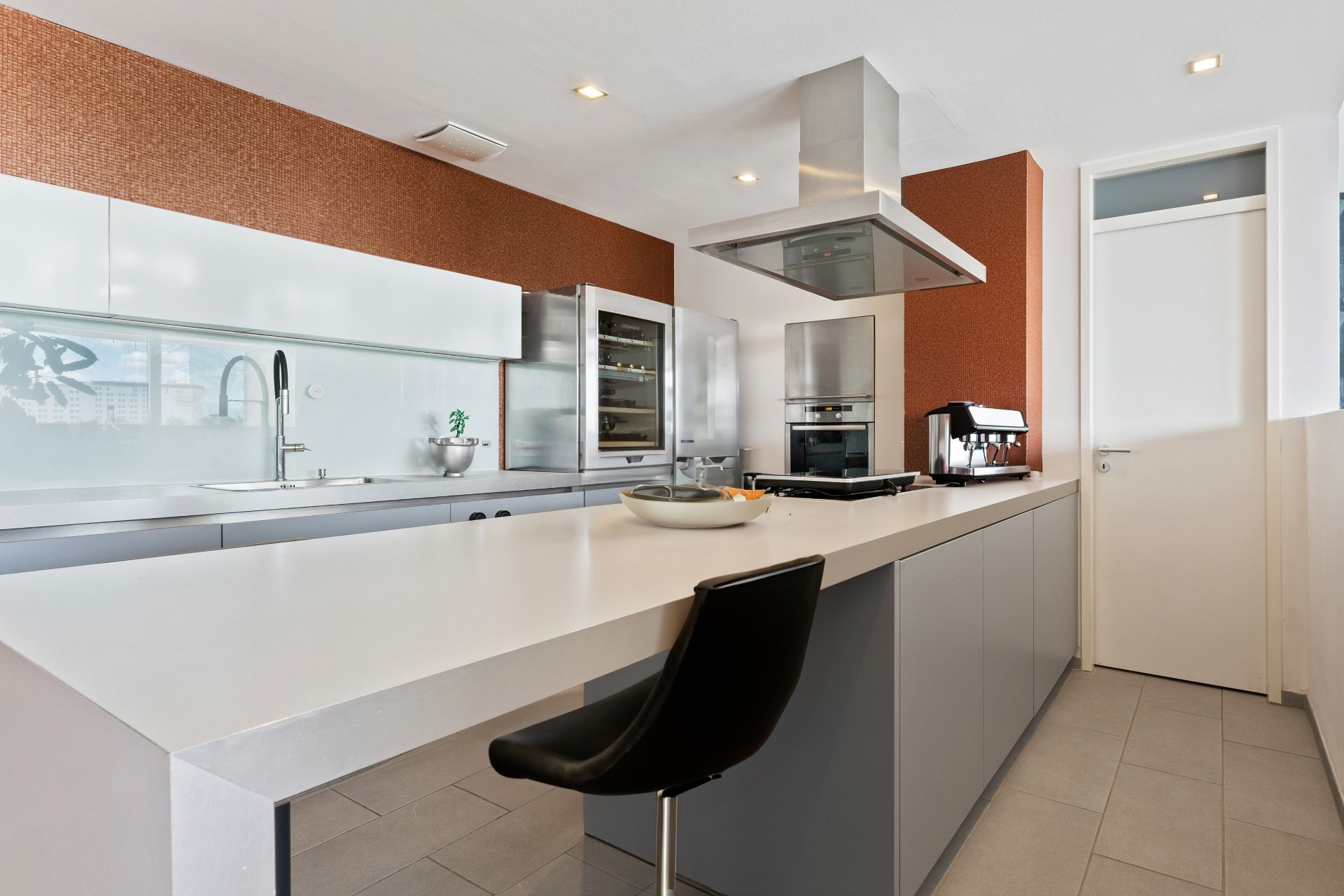 Moderne Küche mit Kücheninsel, Barhocker, Backofen, Kühlschrank und Kaffeemaschine.
