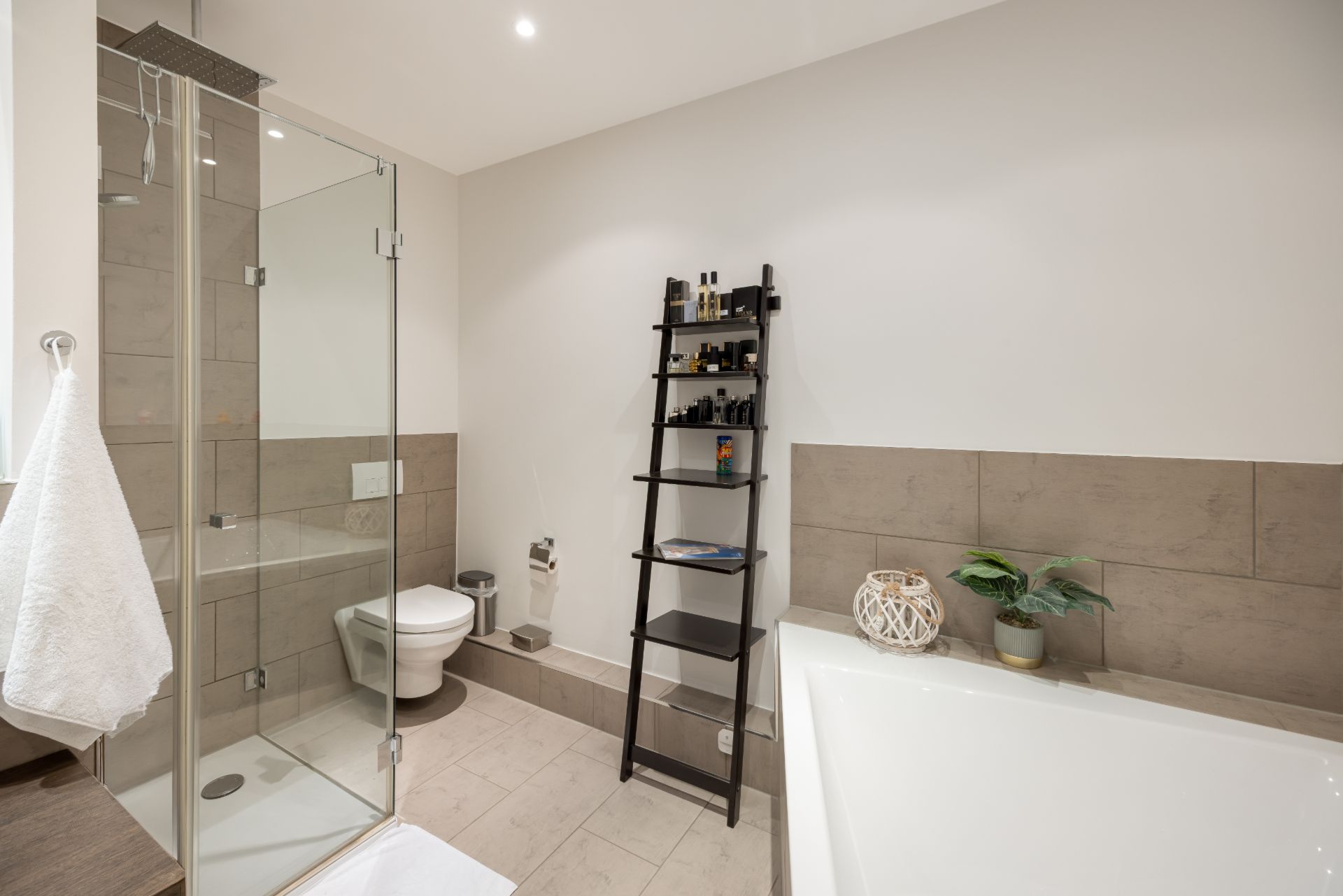 Modernes Badezimmer mit Dusche, Toilette, Badewanne und schwarzem Regal an der Wand.