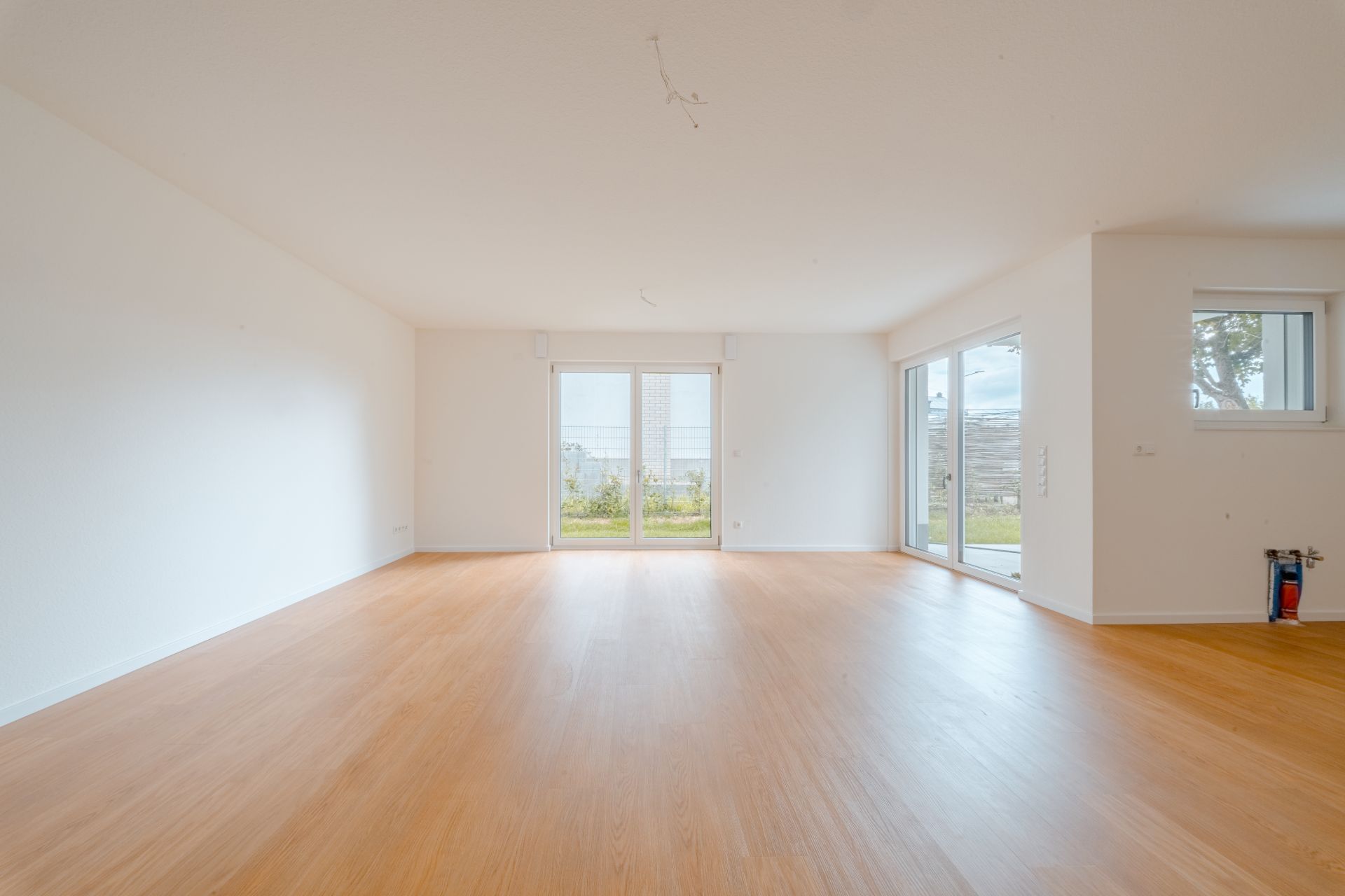 Heller, leerer Raum mit Holzfußboden und großen Fenstern zur Terrasse.