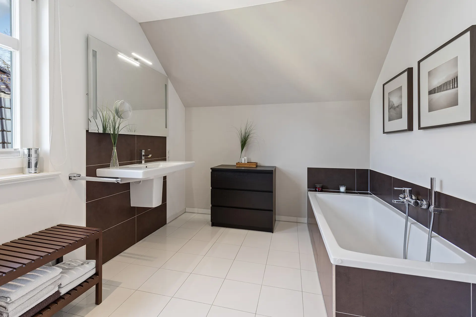 Modernes Badezimmer mit Badewanne, Waschbecken, Kommode und Holzbank mit Handtüchern.