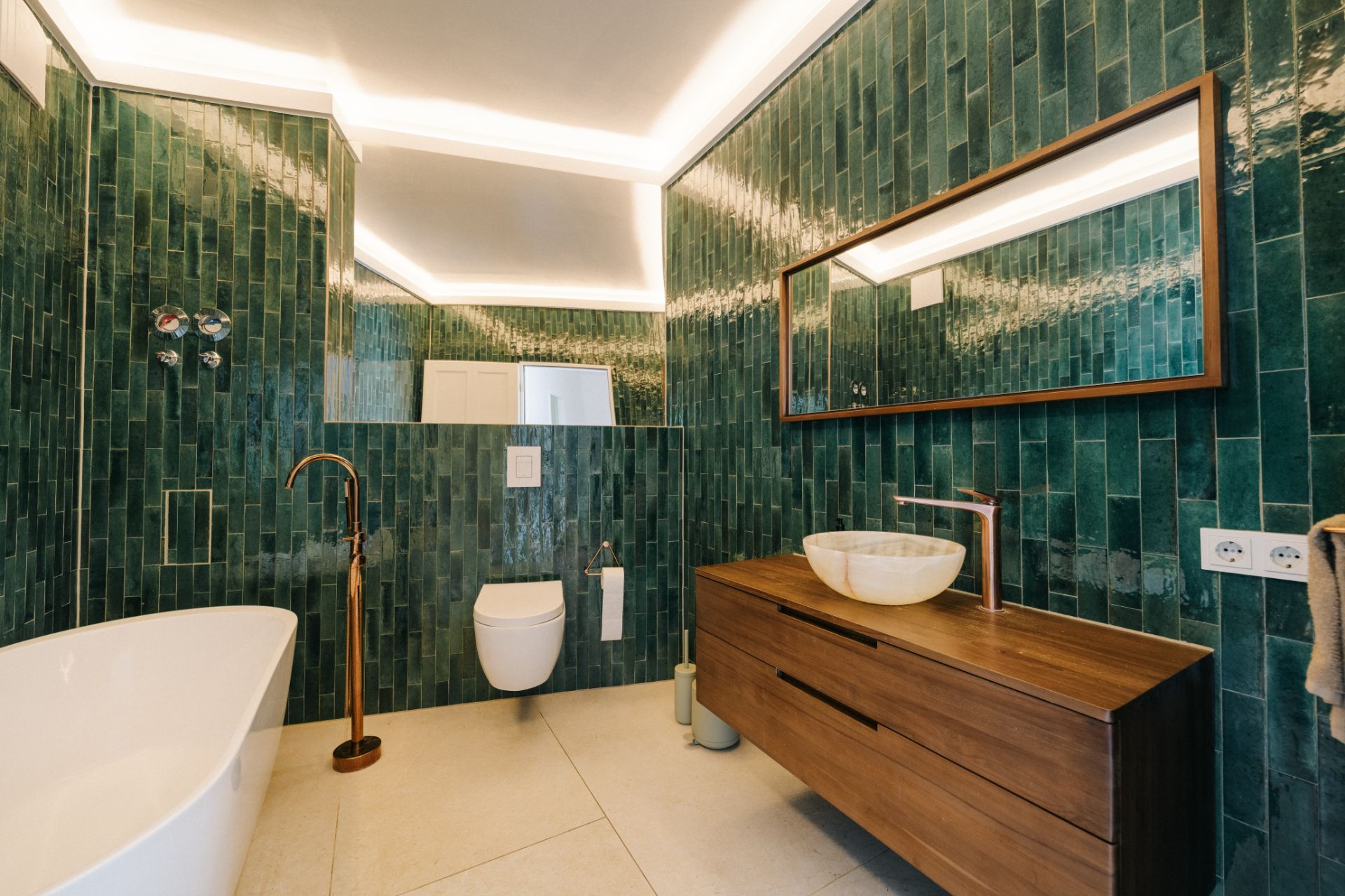 Modernes Bad mit grünen Fliesen, freistehender Badewanne, WC und Holzwaschtisch mit großem Spiegel.