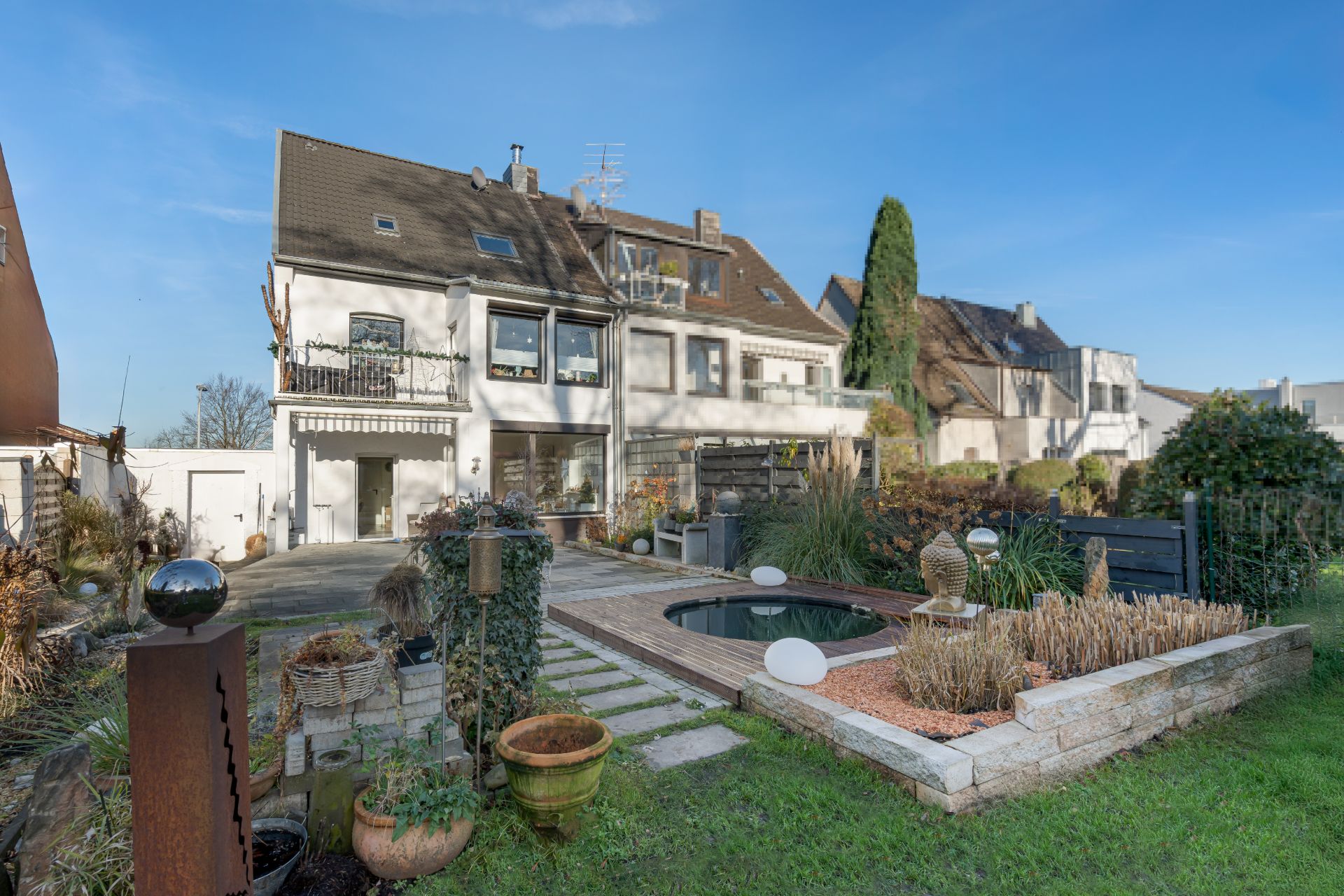 Garten mit kleinem Teich, Terrasse und Pflanzen hinter einem mehrstöckigen Wohnhaus.