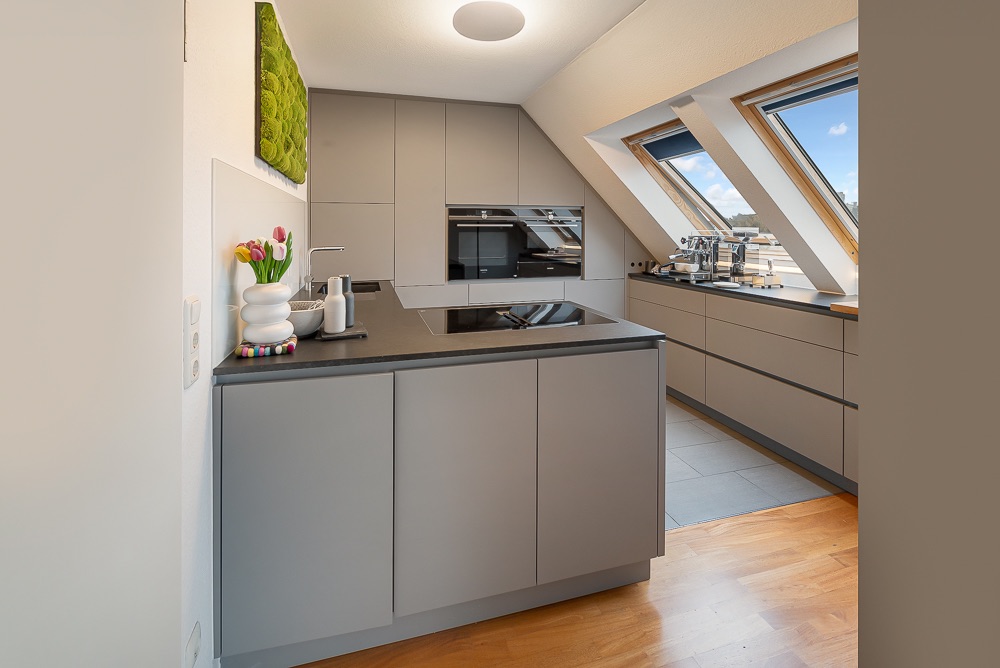 Moderne Küche mit grauen Schränken, Kochinsel und Dachfenstern.