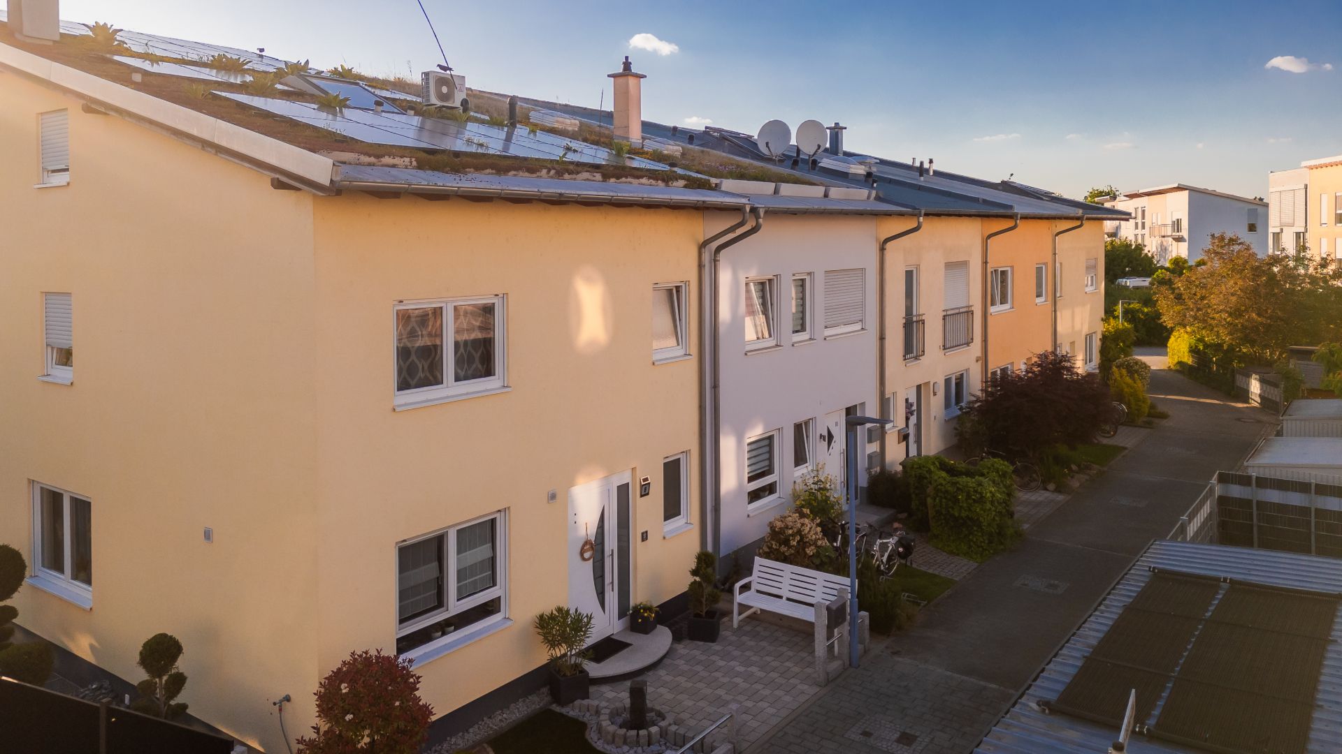Reihenhaus mit gelber und weißer Fassade, Solaranlagen auf dem Dach und Vorgärten.
