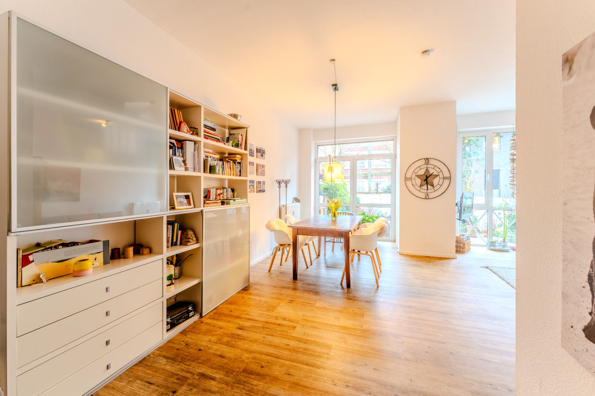 Heller Essbereich mit Holzfußboden, Tisch, vier Stühlen, Regal und großen Fenstern.