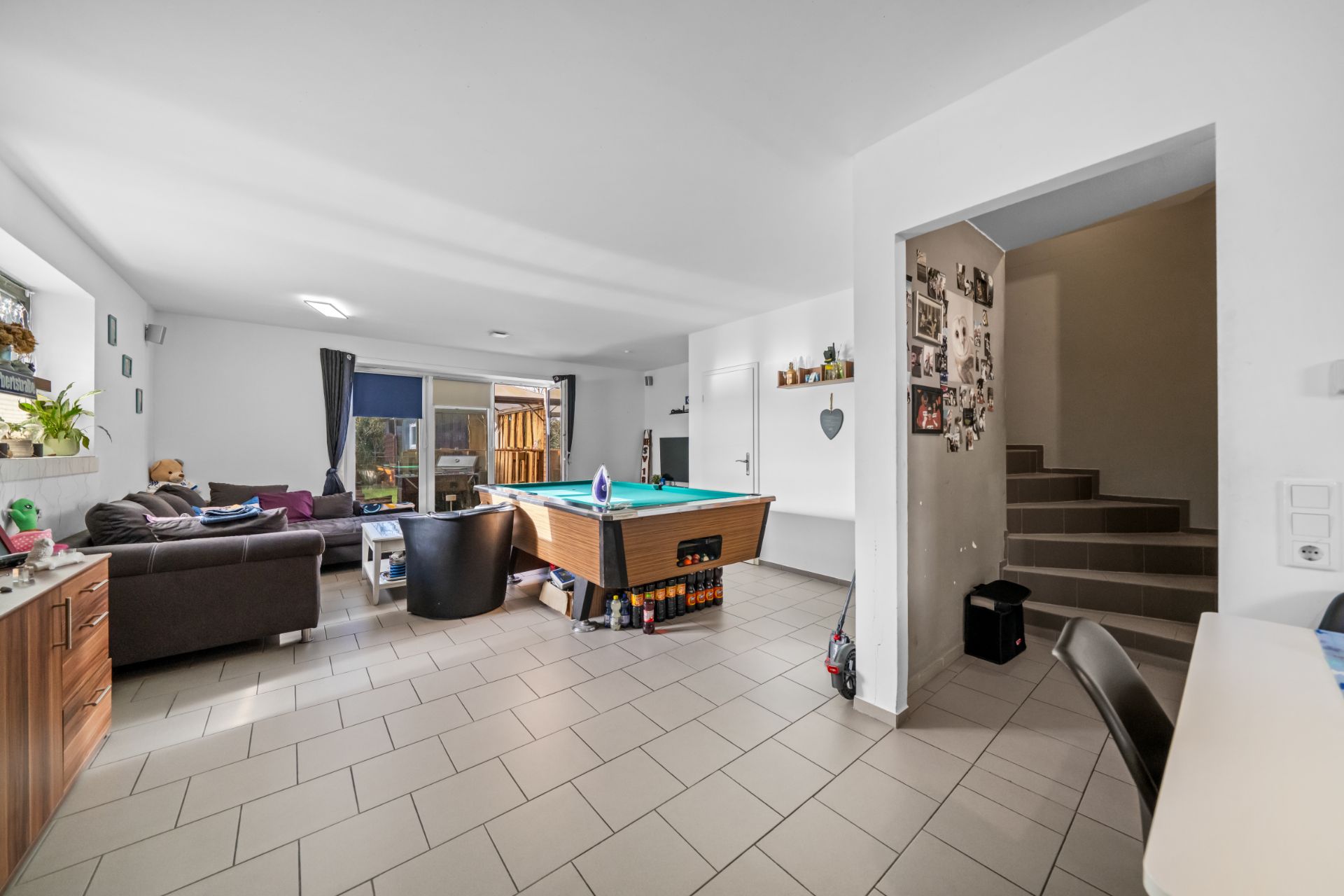 Helles Wohnzimmer mit Sofa, Billardtisch, Stühlen, Treppe und Zugang zum Garten.