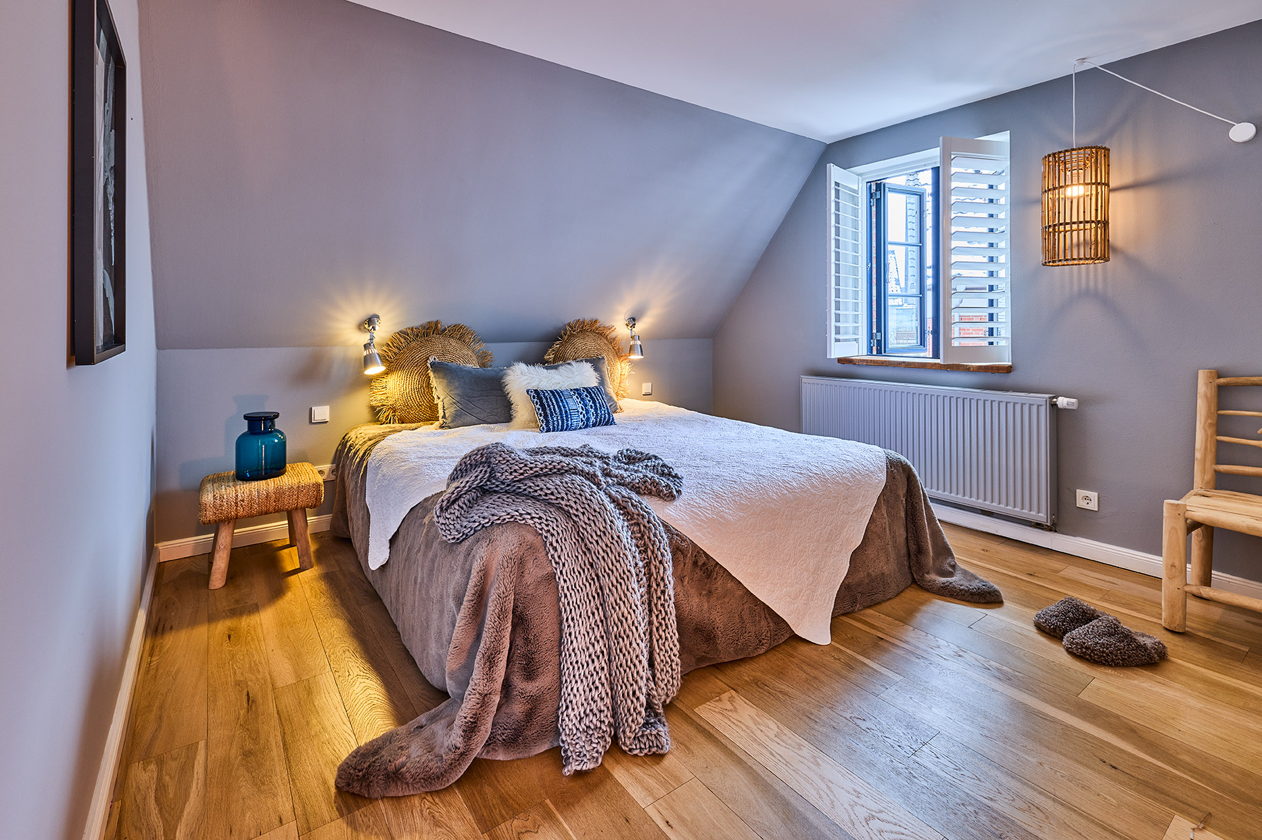 Gemütliches Schlafzimmer mit Doppelbett, Holzboden, offenem Fenster und Nachttisch mit blauer Vase.