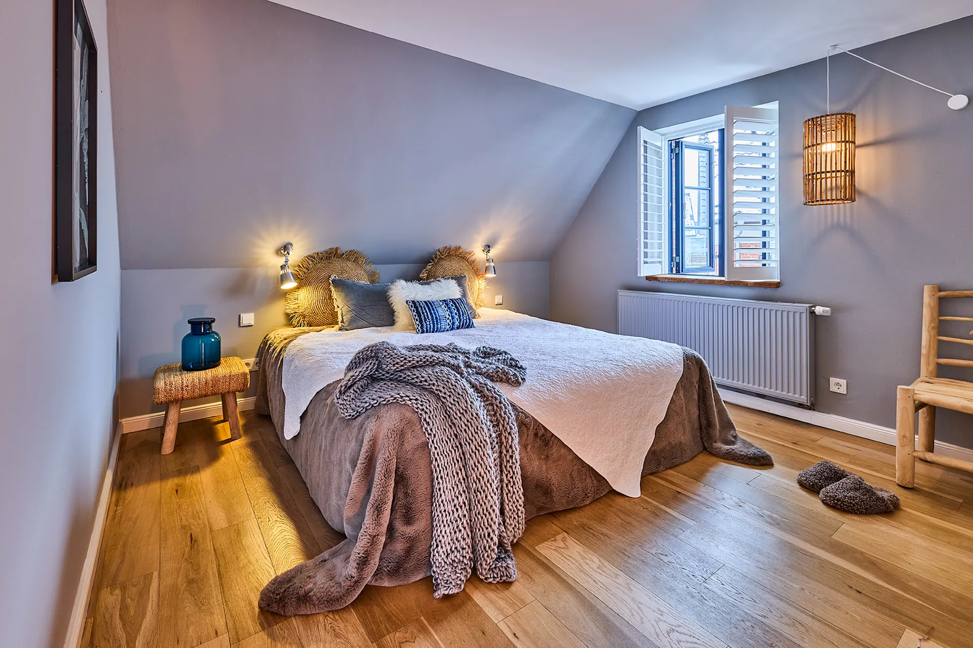 Gemütliches Schlafzimmer mit Doppelbett, Holzboden, offenem Fenster und Nachttisch mit blauer Vase.