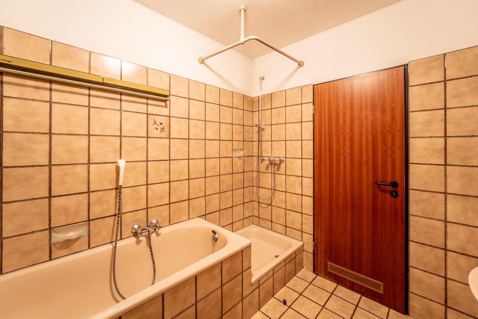 Badezimmer mit beiger Badewanne, Dusche und braunen Fliesen an Wand und Boden.
