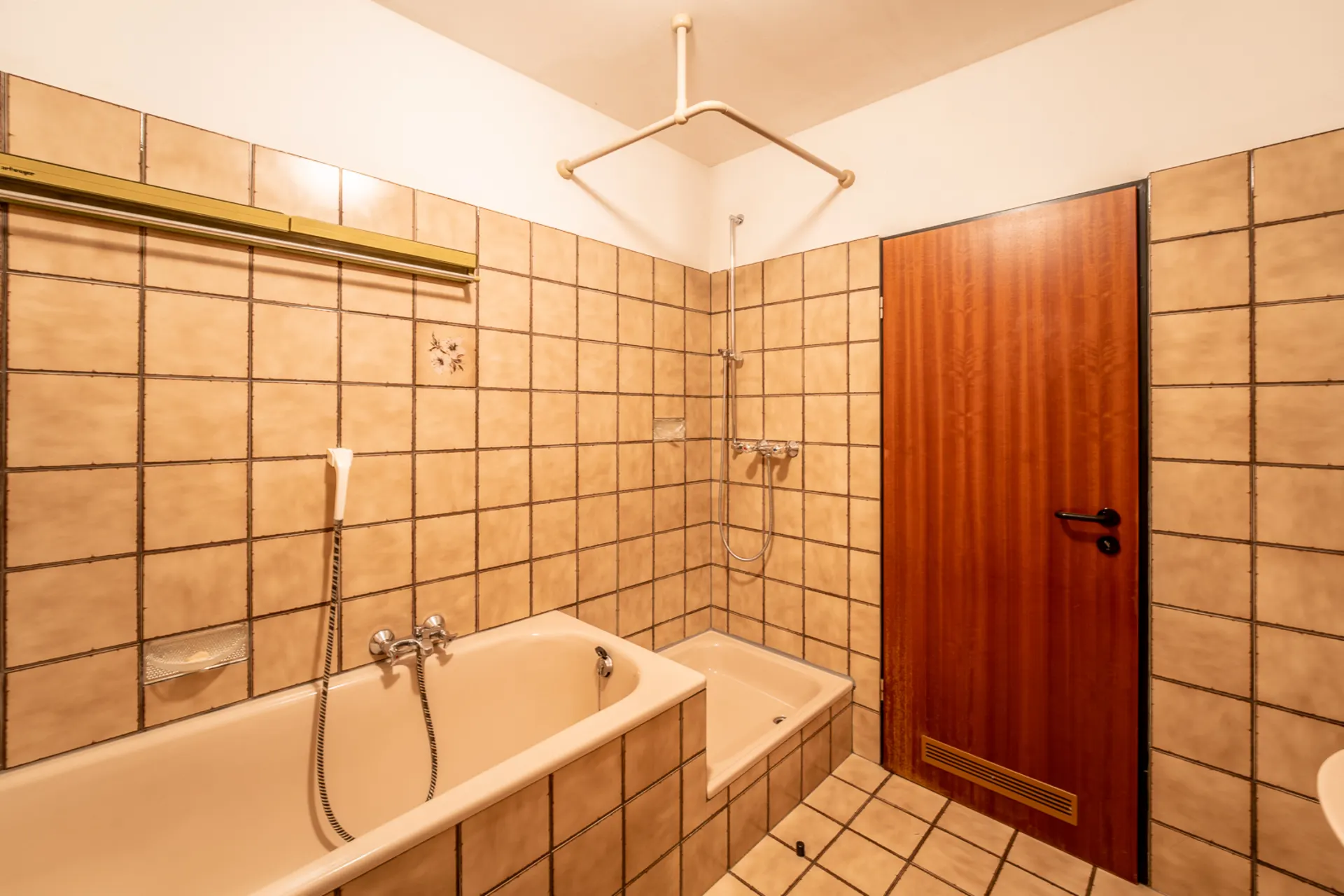 Badezimmer mit beiger Badewanne, Dusche und braunen Fliesen an Wand und Boden.