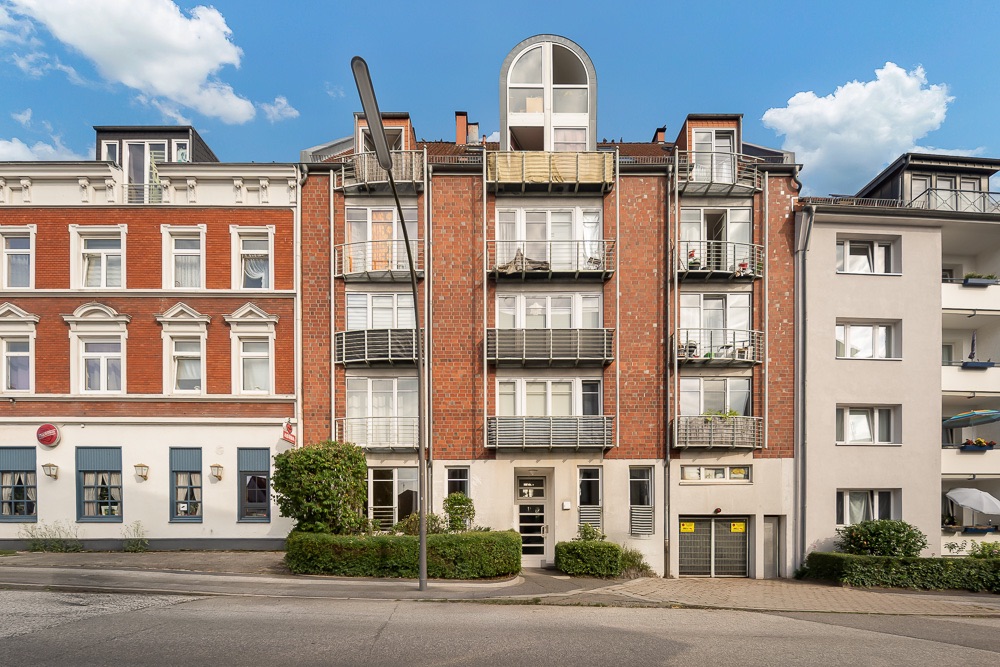 Mehrstöckiges Wohnhaus mit Balkonen und roter Klinkerfassade, zentraler Hauseingang.