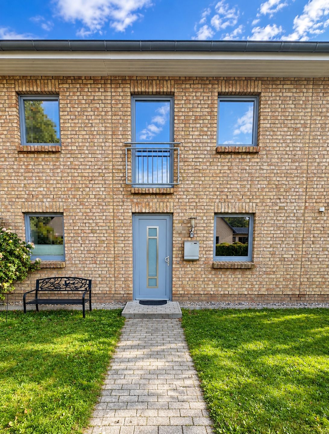Eingang eines Backsteinhauses mit blauer Tür, Bank und kleinem Vorgarten.
