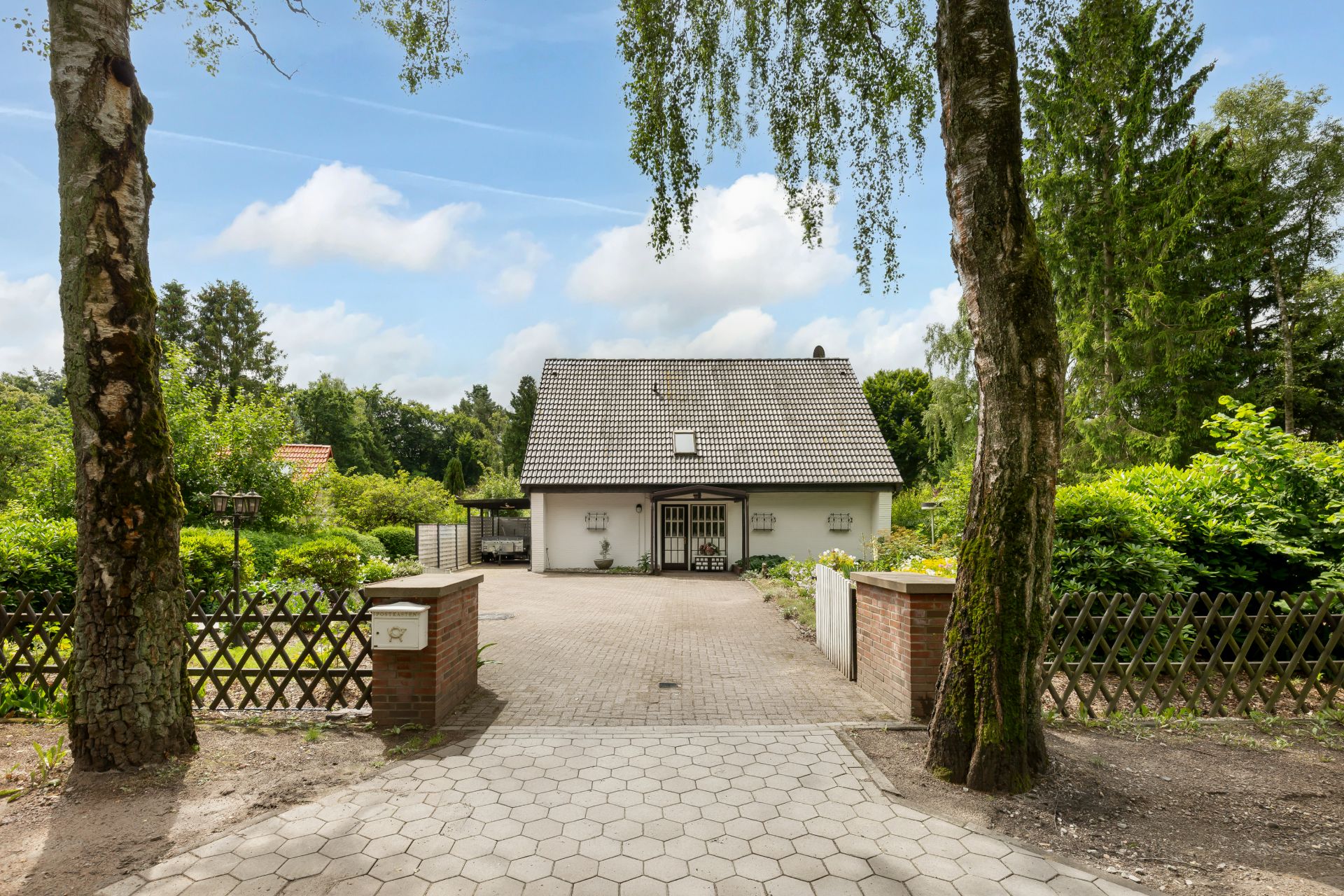 Einfamilienhaus mit Satteldach, gepflasterte Einfahrt, umgeben von Garten und Bäumen.