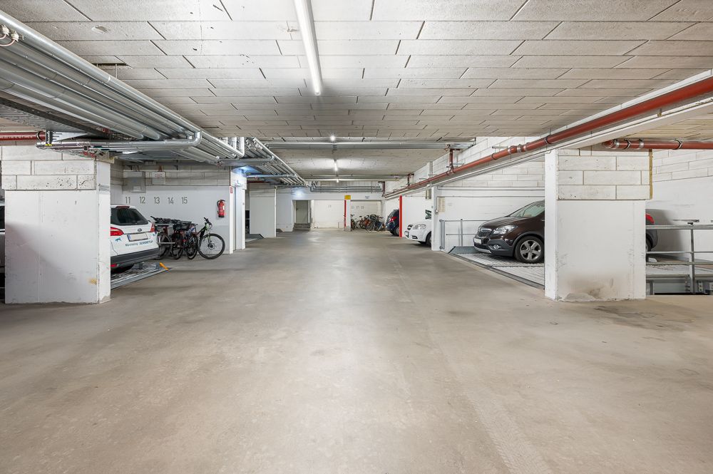 Helle Tiefgarage mit parkenden Autos und einigen Fahrrädern an den Seiten.