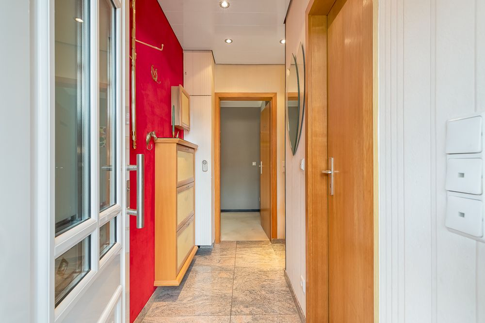 Heller Flur mit roter Wand, Holzkommode und mehreren Türen.