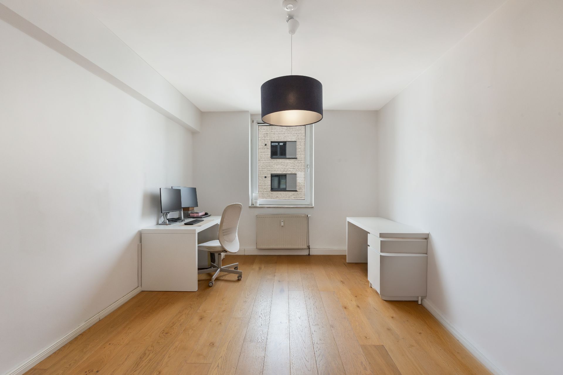 Helles Arbeitszimmer mit Holzfußboden, Schreibtischen, Stuhl und einem Fenster in der Mitte.