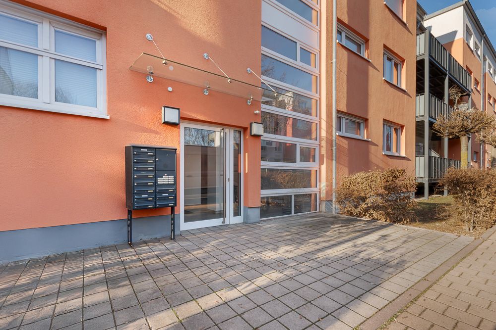 Eingang eines Wohnhauses mit Glas-Schiebetür, Briefkästen und oranger Fassade.