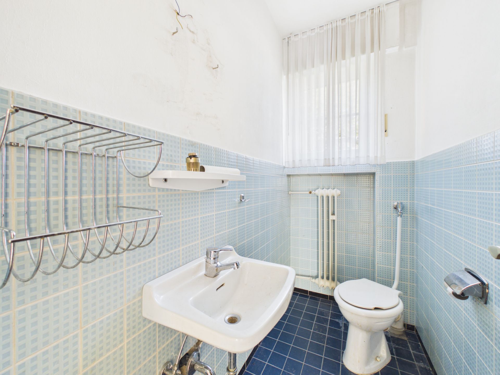 Kleines Badezimmer mit Waschbecken, Toilette, Handtuchhalter und blau gefliesten Wänden.