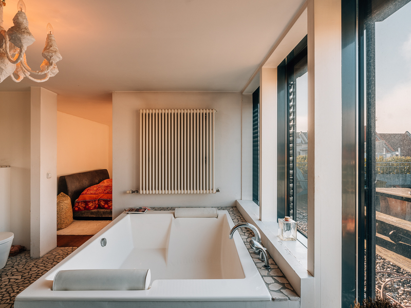 Helles Badezimmer mit großer Badewanne, Heizkörper und großen Fenstern zum Garten.