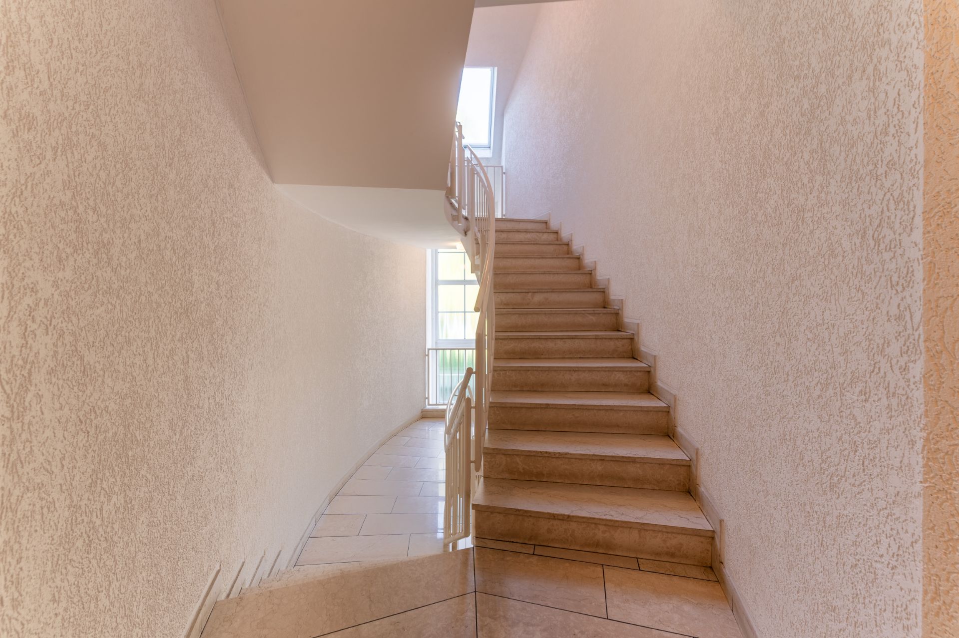 Helle Treppe mit cremefarbenen Wänden und Fliesenboden, Tageslicht durch Fenster.