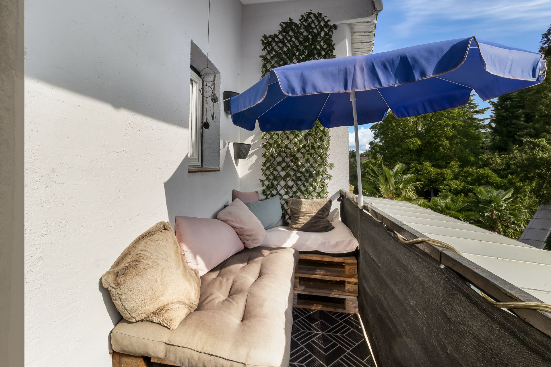 Kleiner Balkon mit Sitzbank, bunten Kissen und blauem Sonnenschirm.