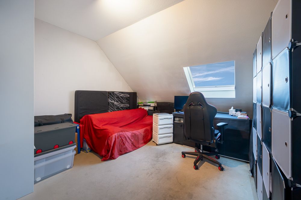 Zimmer mit rotem Sofa, Schreibtisch, Stuhl, Regal und Dachfenster.