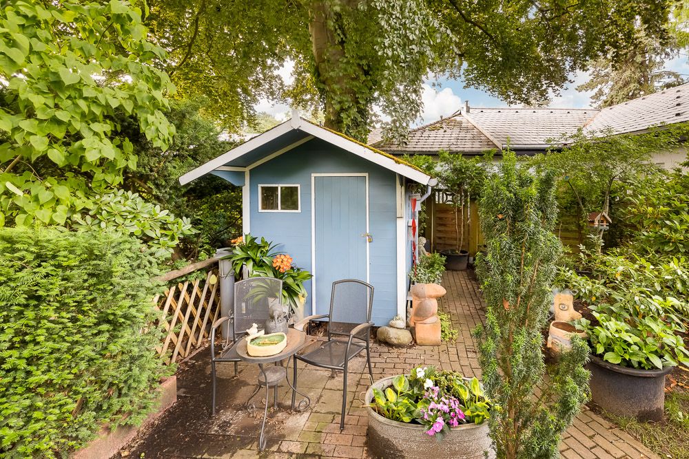 Kleines blaues Gartenhaus mit Sitzbereich und vielen Pflanzen im Grünen.