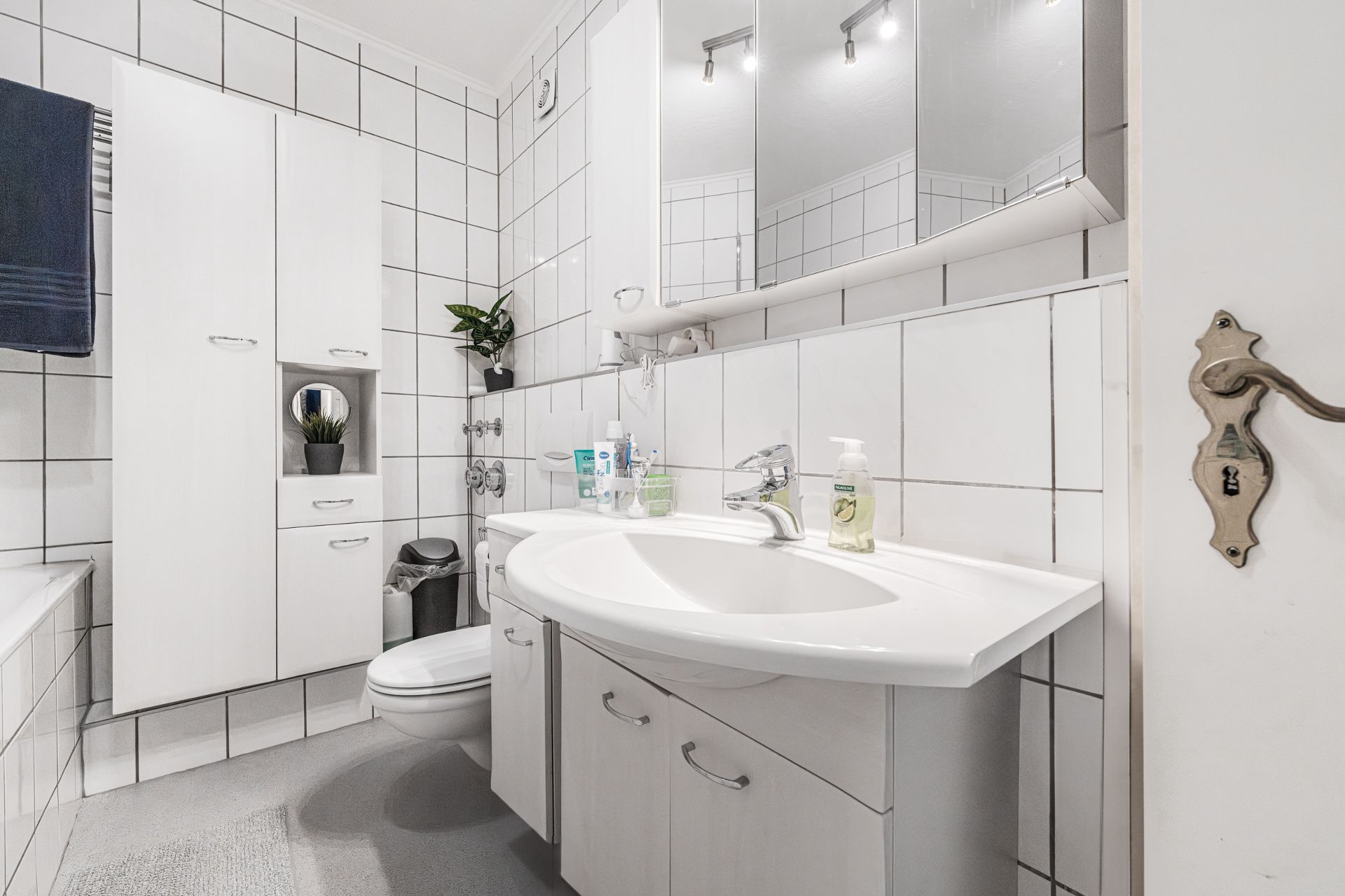 Modernes Badezimmer mit weißem Waschbecken, Spiegelschrank und weißen Fliesen.