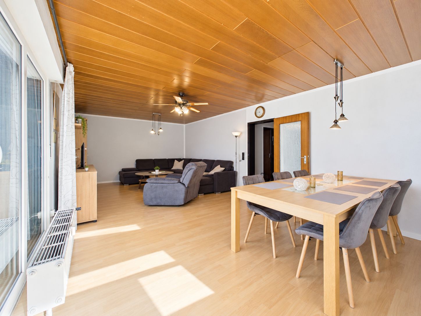 Helles Wohn- und Esszimmer mit Holzboden, Esstisch, Stühlen und großer Sofaecke.