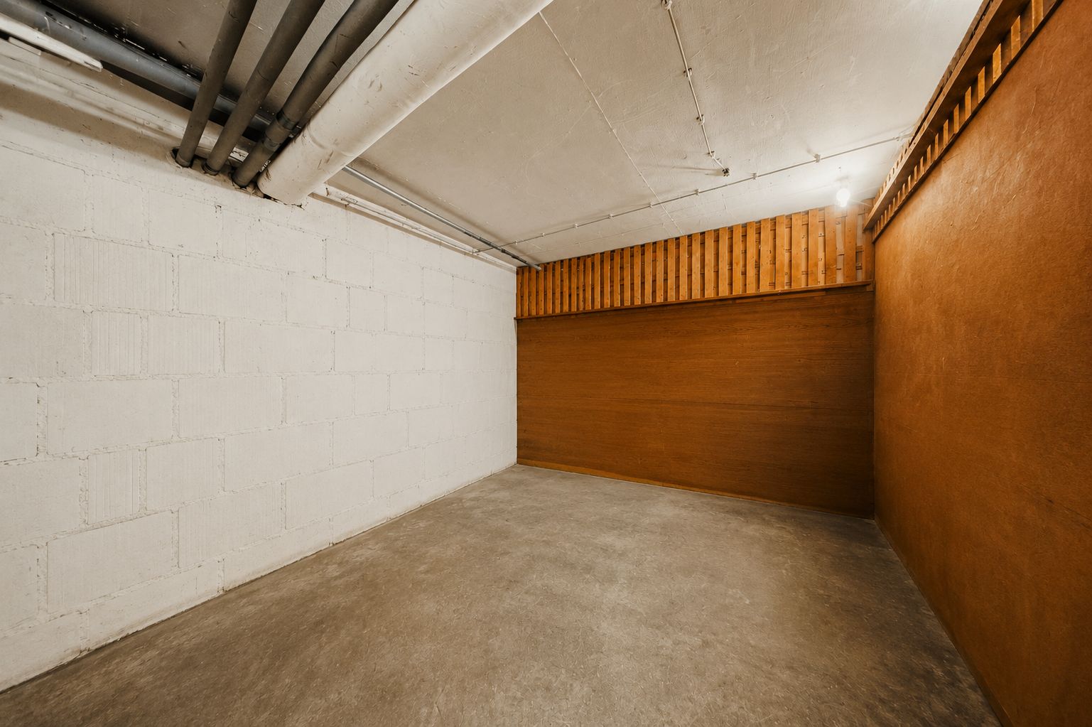Leerer Raum mit Betonboden, weißer Backsteinwand und braunen Holzwänden.