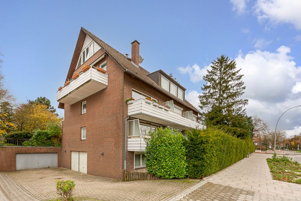 Backsteinwohnhaus mit mehreren Balkonen, umgeben von Bäumen und einer gepflasterten Einfahrt.