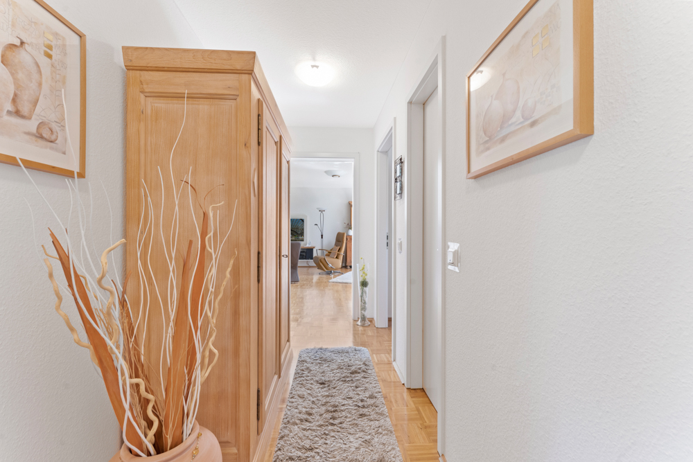 Heller Flur mit Teppich, Holzschrank, Trockenpflanzen und Bildern an den Wänden.