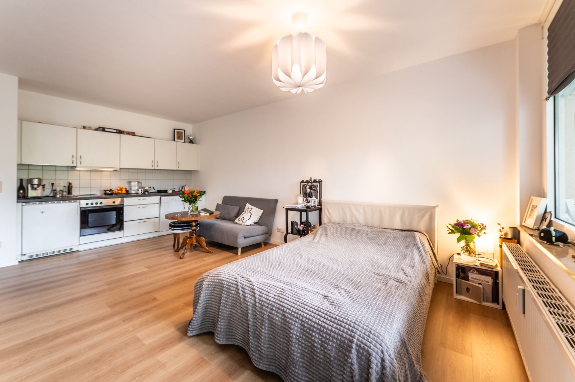 Helles Studio mit Küche, Bett, Sofa, Holzboden und großem Fenster.