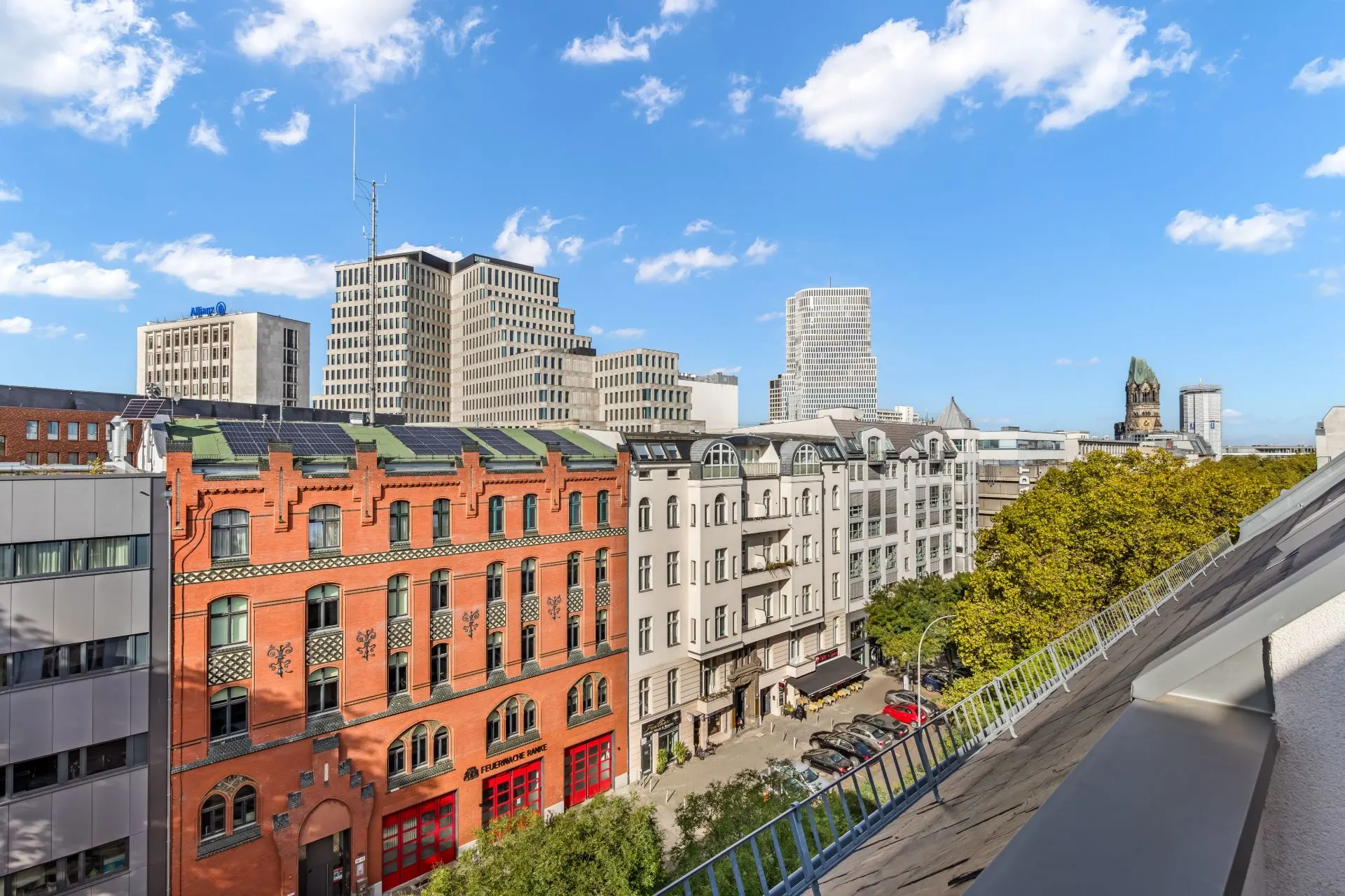 Blick von einem Balkon auf eine Straße mit Wohngebäuden und modernen Hochhäusern im Hintergrund.