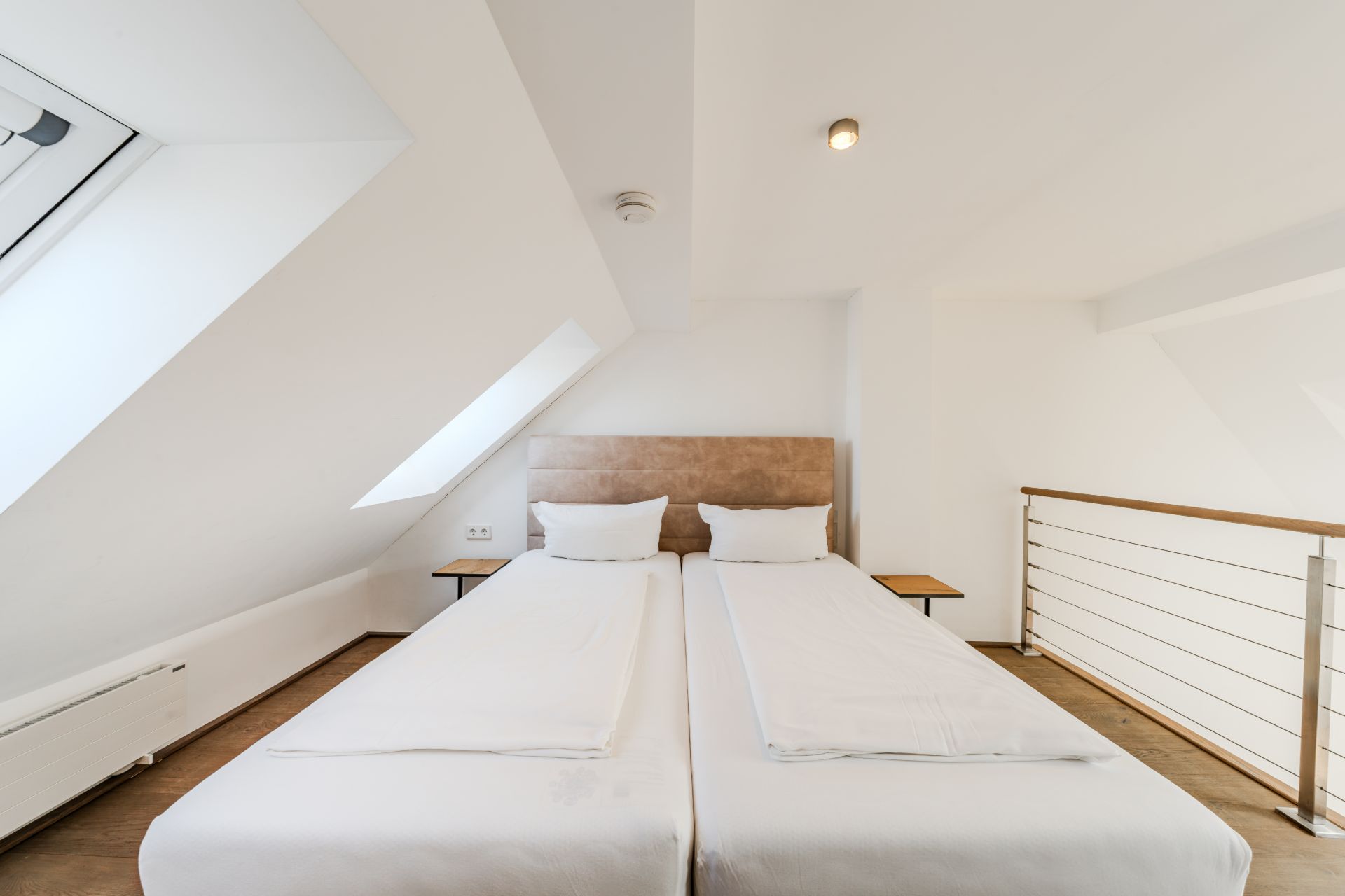 Dachzimmer mit zwei Einzelbetten, Nachttischen und Fenster.