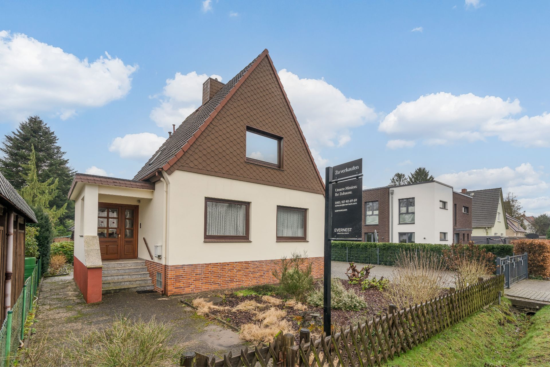 Einfamilienhaus mit Garten, Vorgartenzaun, Verkaufsschild und Eingangsbereich mit Treppe.