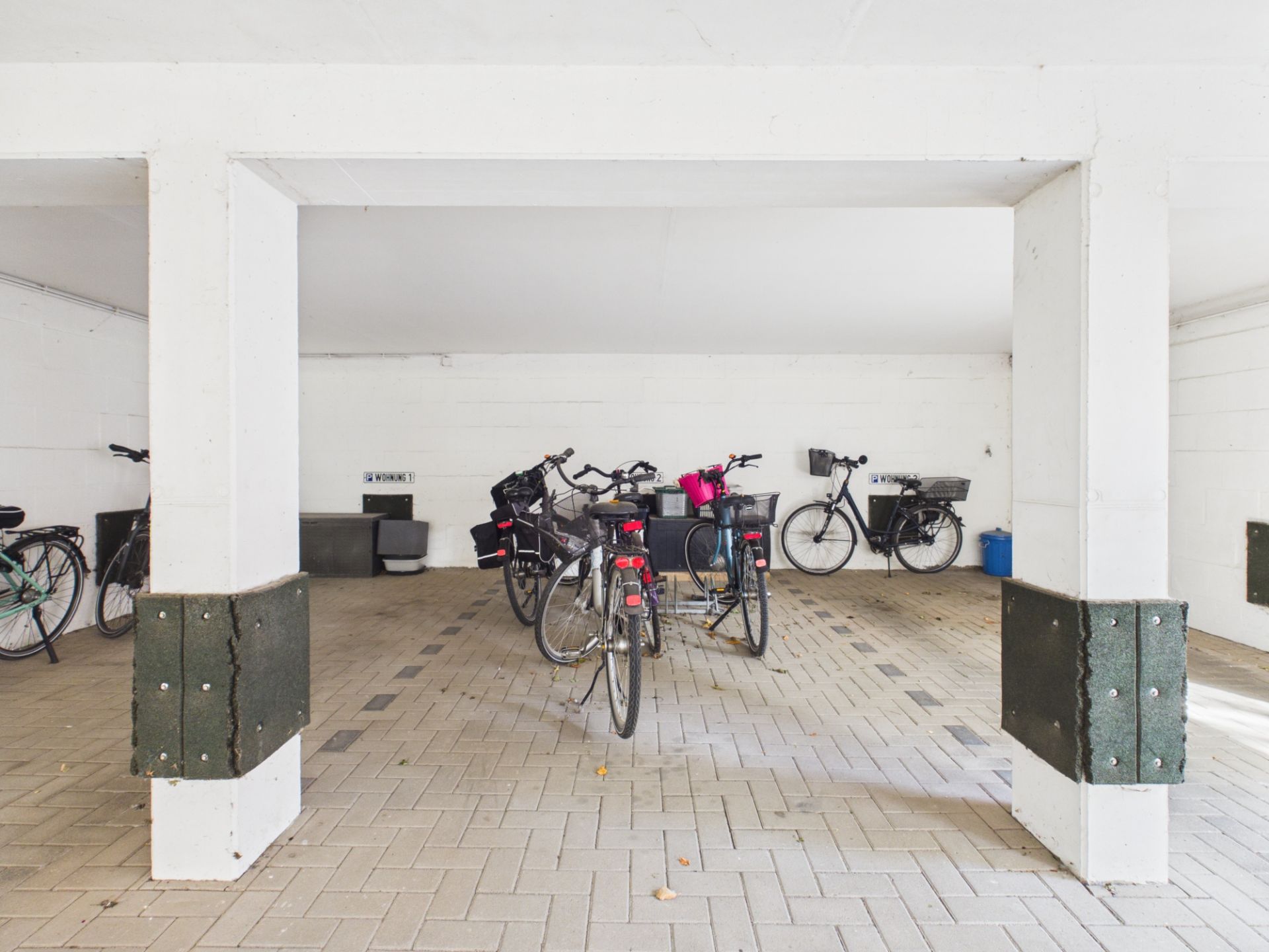Überdachter Fahrradabstellraum mit mehreren geparkten Fahrrädern auf Pflastersteinen.