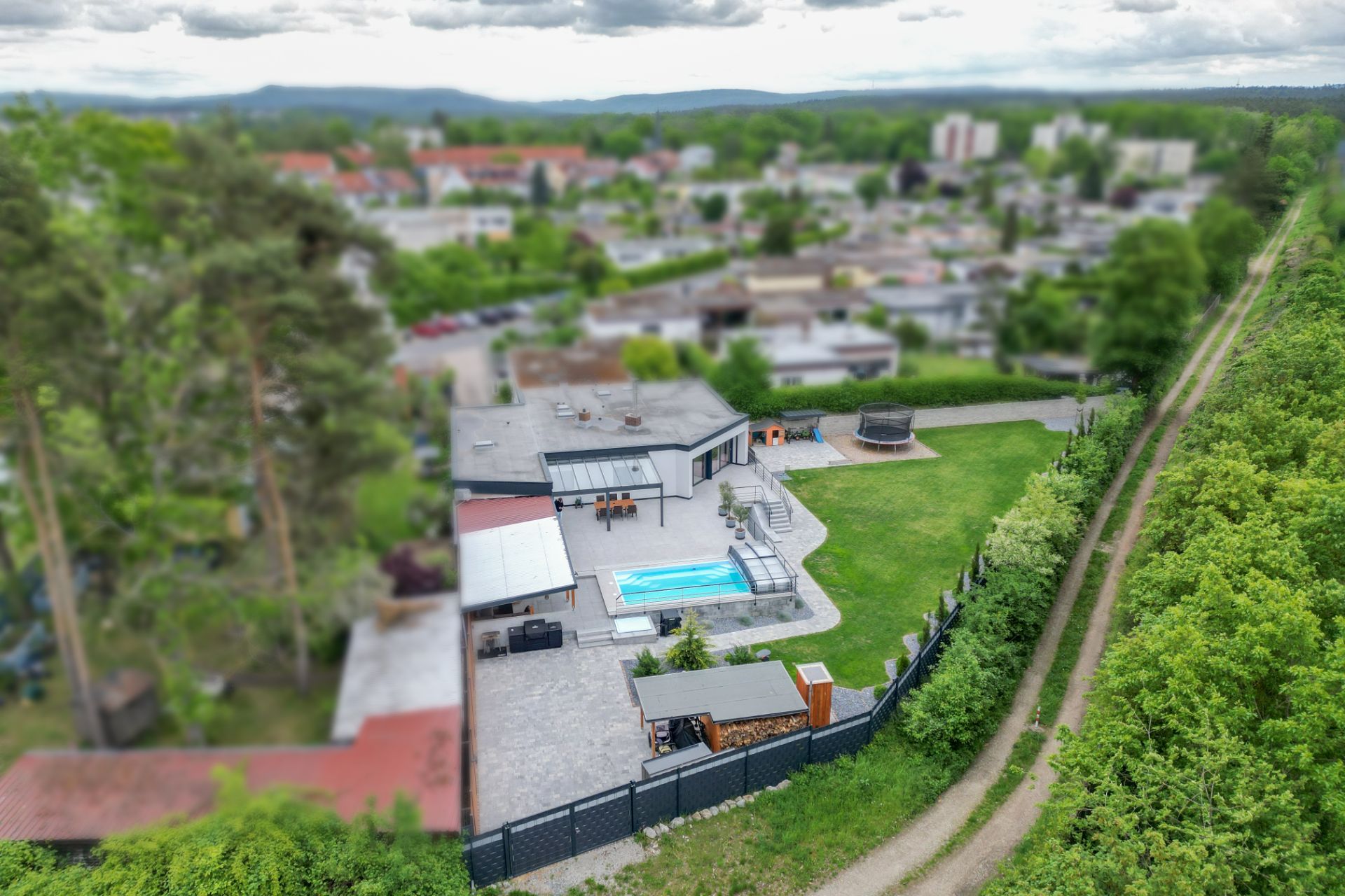 Luftaufnahme eines Wohnhauses mit Garten, Pool und Terrasse, umgeben von Bäumen und Wegen.