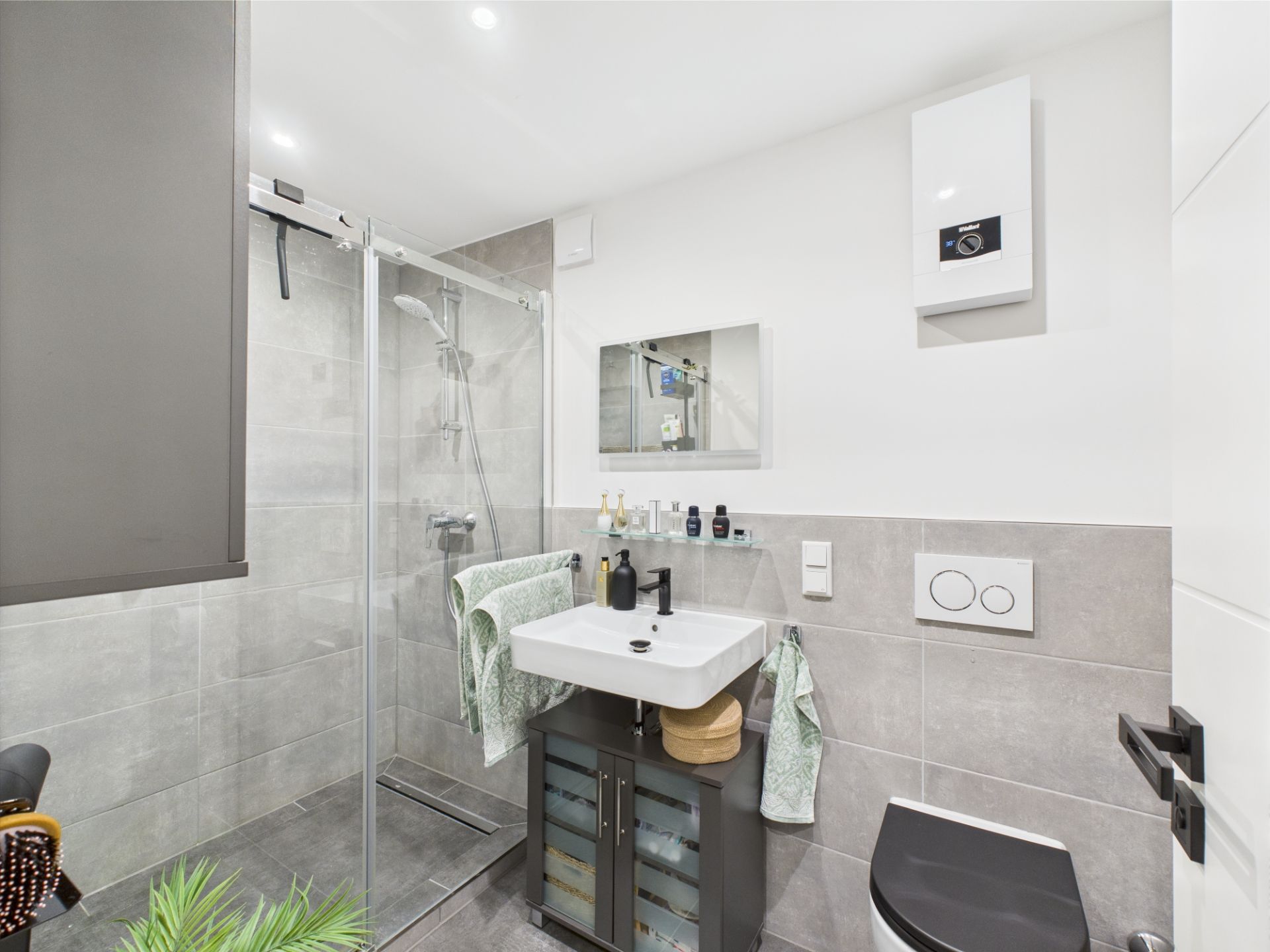 Modernes Badezimmer mit Dusche, Waschbecken, Spiegel und Toilette, graue Fliesen und helle Wände.