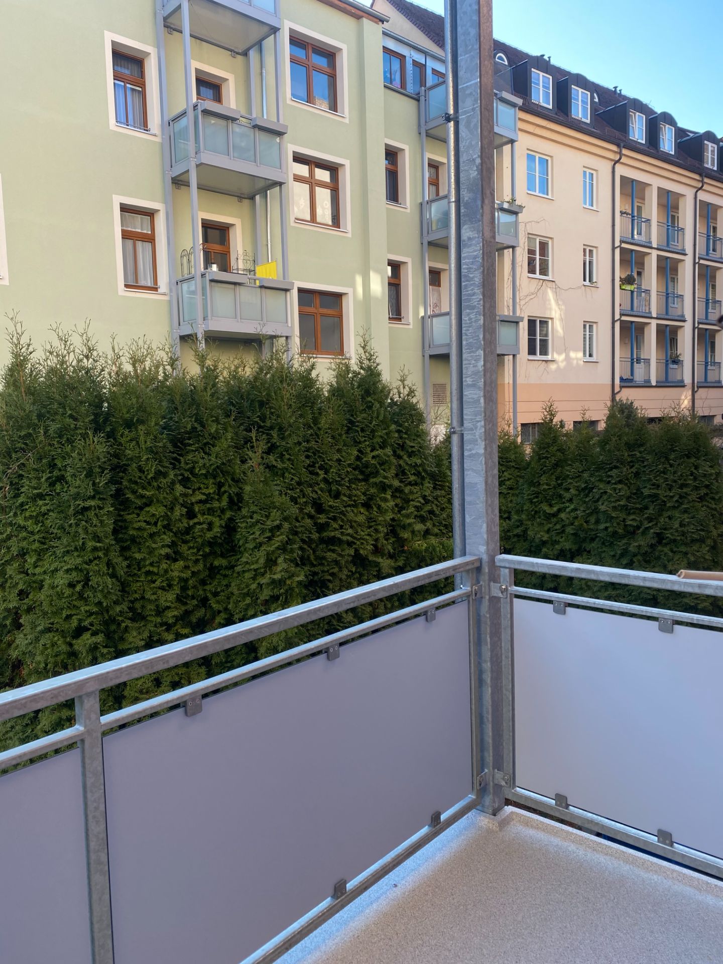 Blick von einem Balkon auf Nachbarhäuser und hohe grüne Hecken.