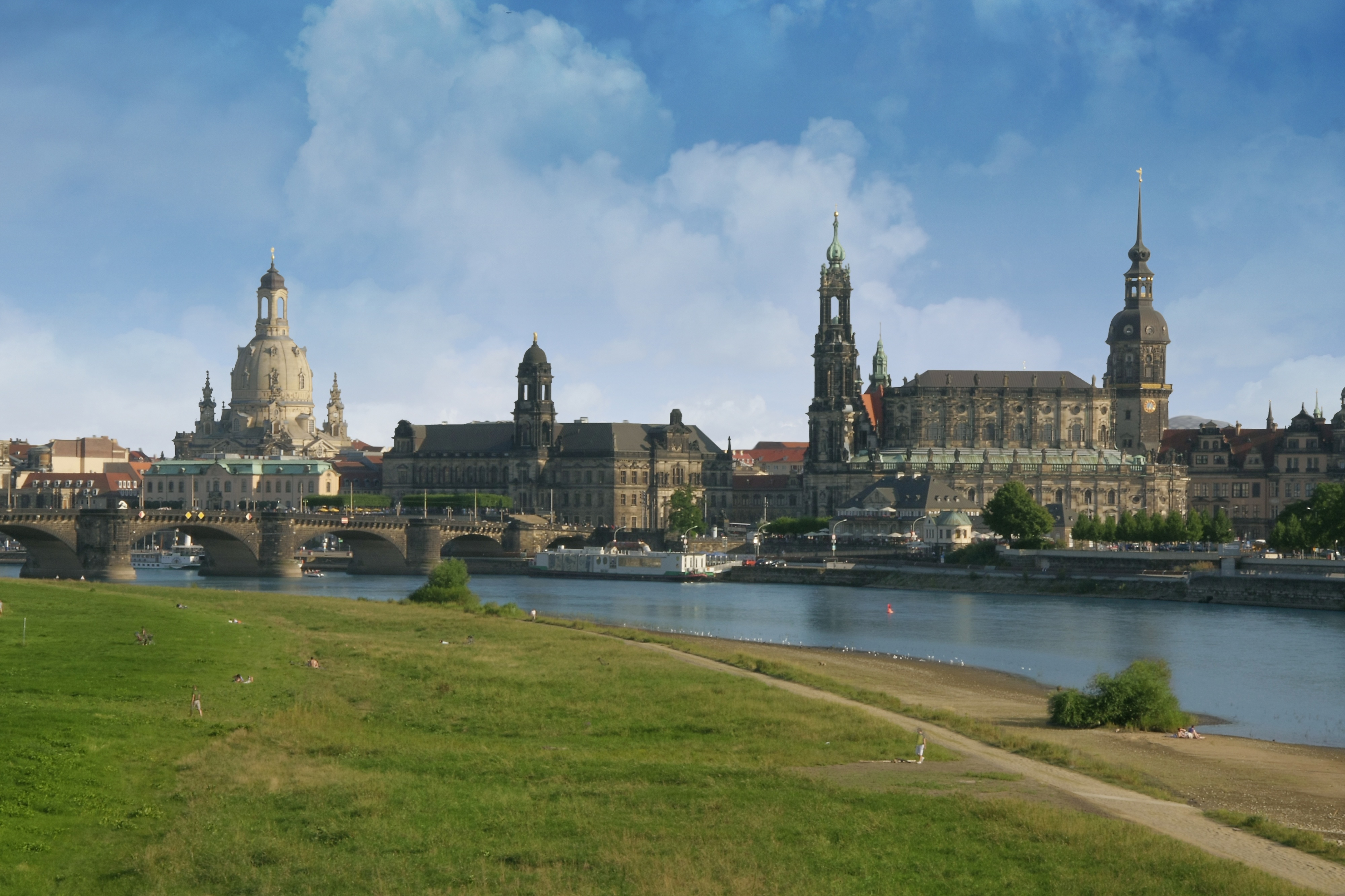 Stadtansicht mit Fluss, historischer Brücke und großen Gebäuden im Hintergrund.