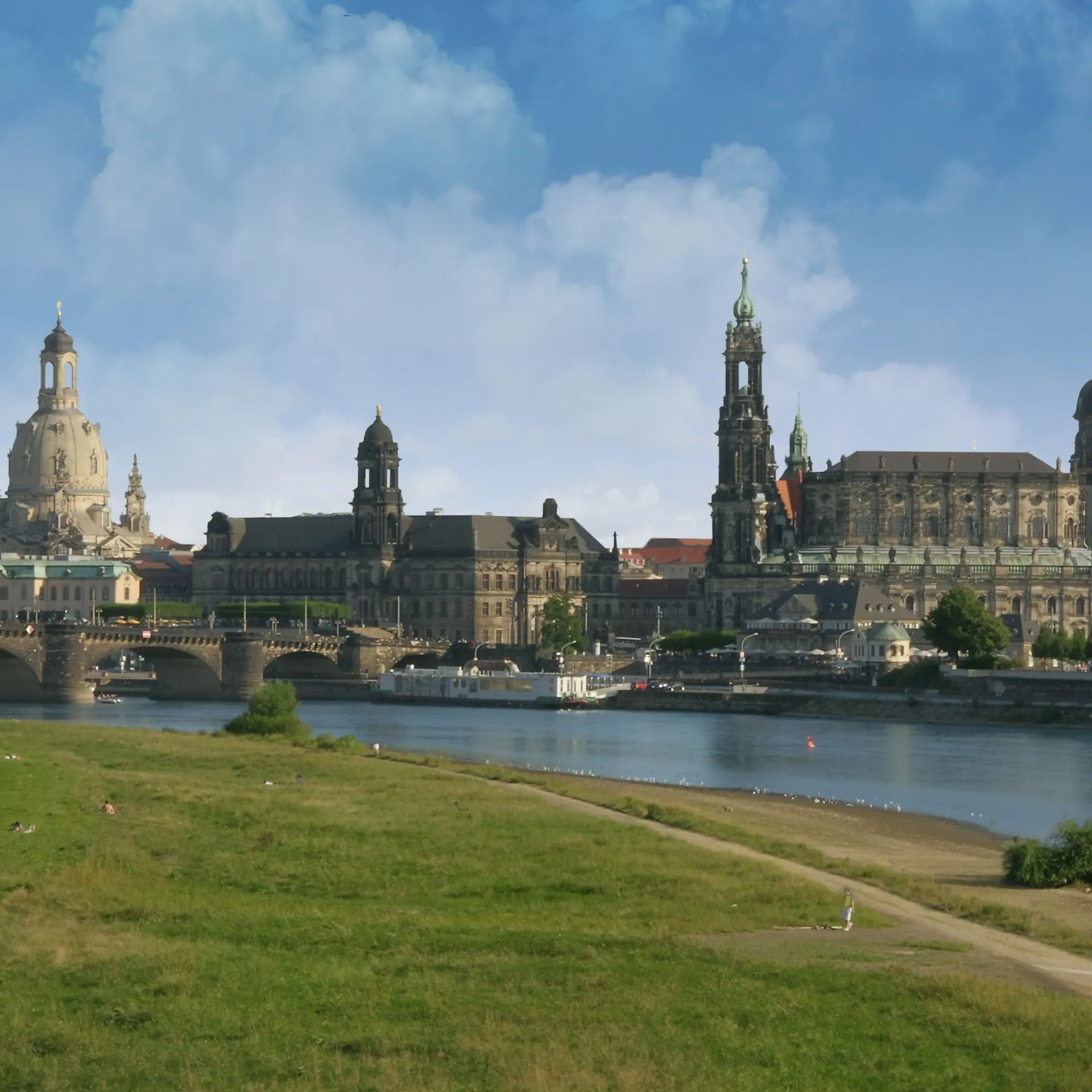 Stadtansicht mit Fluss, historischer Brücke und großen Gebäuden im Hintergrund.