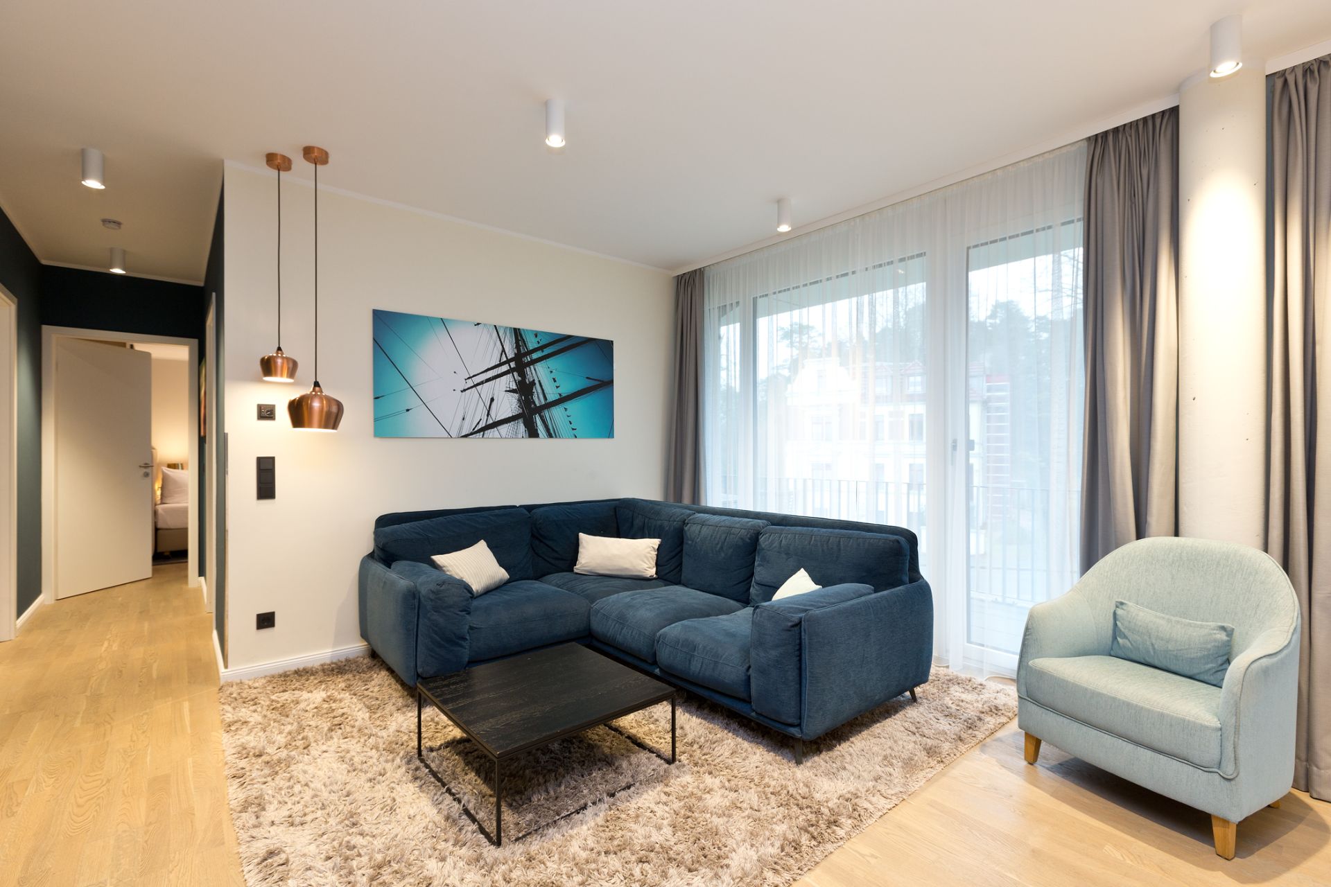 Modernes Wohnzimmer mit blauem Ecksofa, Sessel, Teppich und großem Fenster mit Vorhängen.