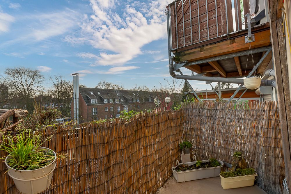 Kleiner Balkon mit Bambusverkleidung und Pflanzkübeln, Ausblick auf Wohnhäuser und blauen Himmel.